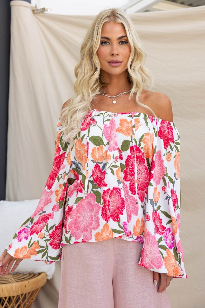 Woman wearing the Delighted Top, a floral off-shoulder blouse with tie detail, perfect for summer styling.