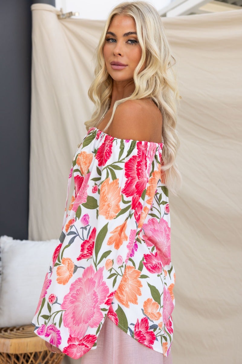 Floral print off-shoulder top with tie detail at bust, model wearing relaxed fit, vibrant colors on a light background.