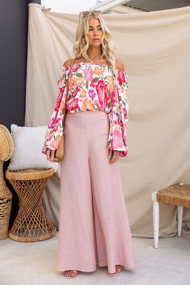 Model wearing a floral print off-shoulder top with tie detail, paired with pink wide-leg pants, showcasing a relaxed summer style.