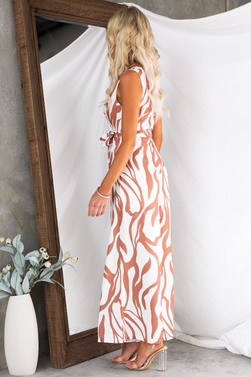 Side view of a girl in a linen blend jumpsuit with a V-neckline and tie waist, styled with wavy patterns.