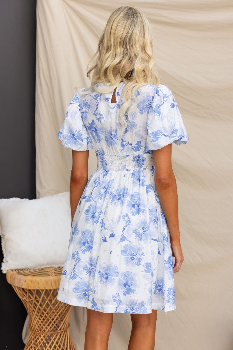 Back view of floral print Already Gone Dress with puff sleeves and elastic waist, featuring a button detail and pockets.