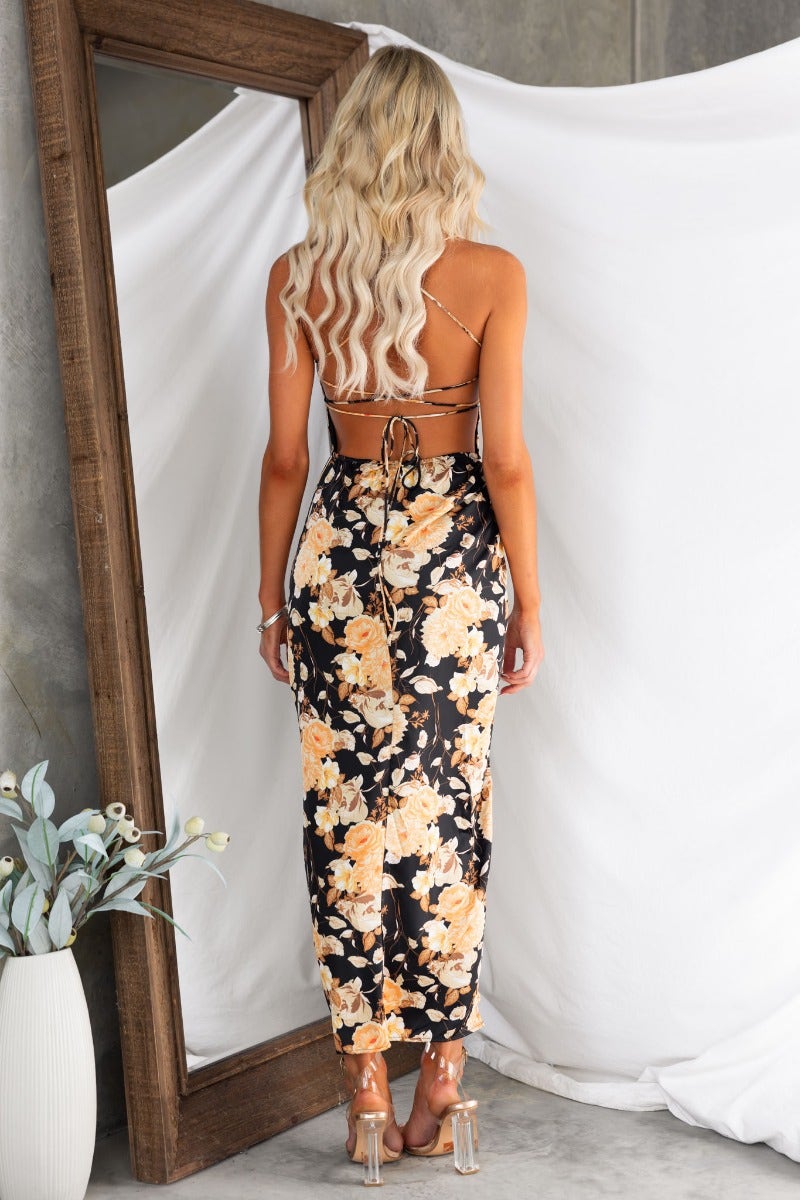 Back view of a woman in a floral maxi dress with adjustable tie straps and cross-over design.