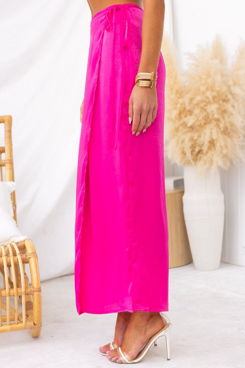 Model wearing a vibrant pink Nerida Wrap Midi Skirt with a fabric tie and asymmetrical hem, styled with elegant heels.