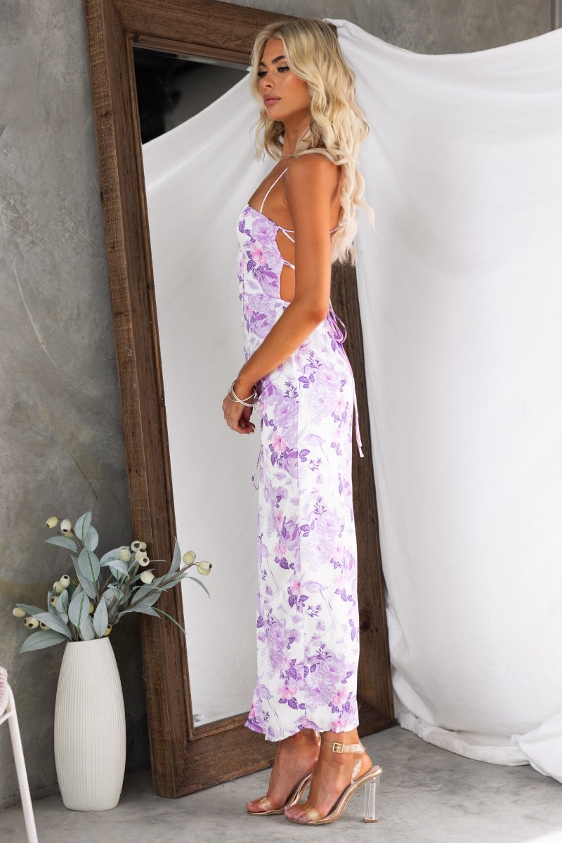 Side view of a woman in a floral satin maxi dress with adjustable tie straps and a cut-out back.