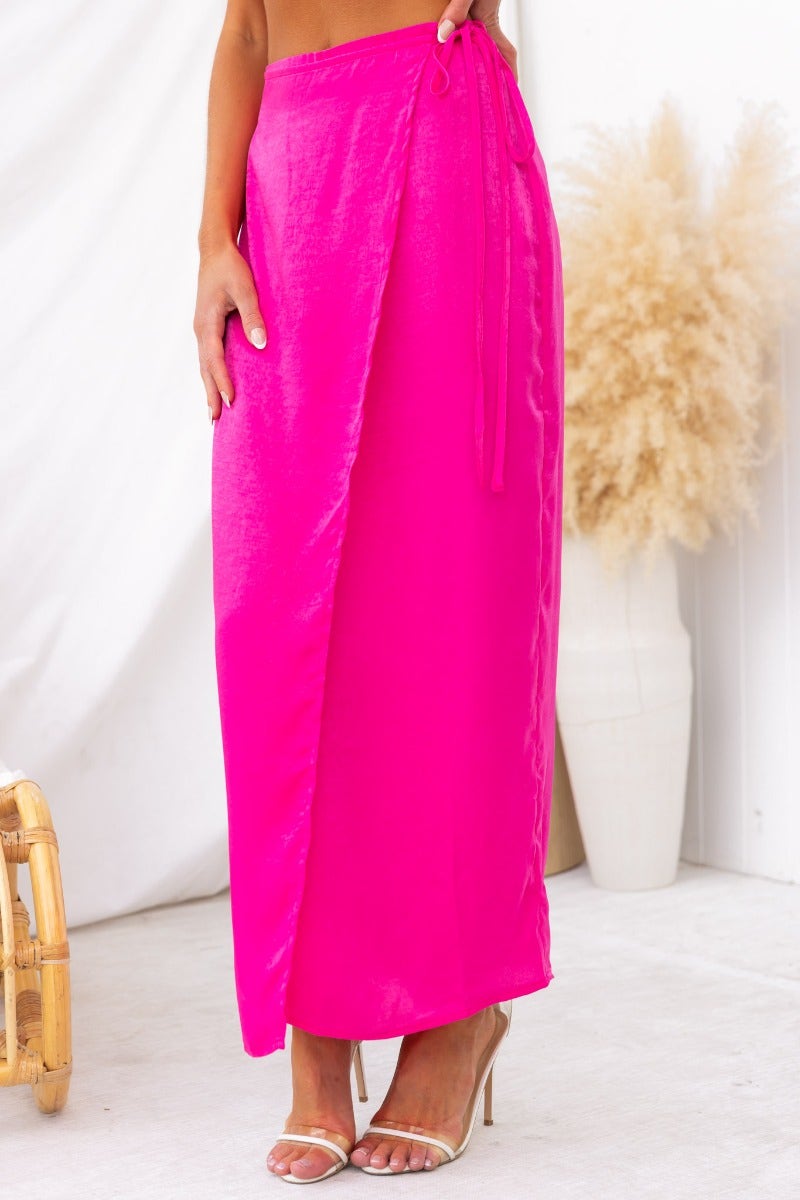 Bright pink Nerida wrap midi skirt with fabric tie and asymmetric hem, styled with elegant heels.
