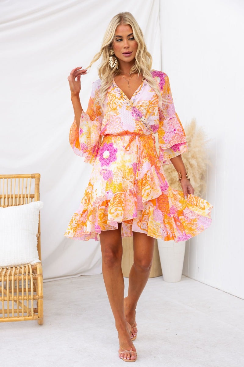 Model in a vibrant Fools Gold Wrap Dress with floral patterns, V-neckline, and ruffled hem.