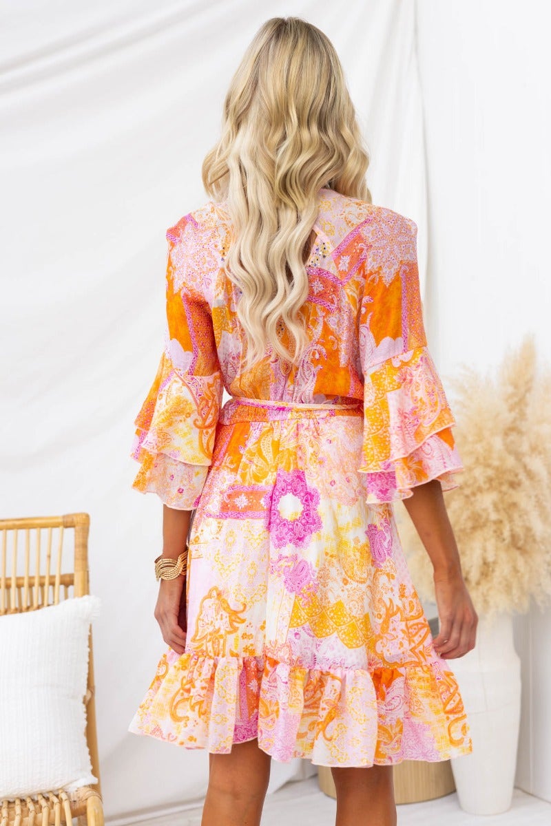 Back view of a woman in a colorful Fools Gold wrap dress with ruffled sleeves and floral patterns.