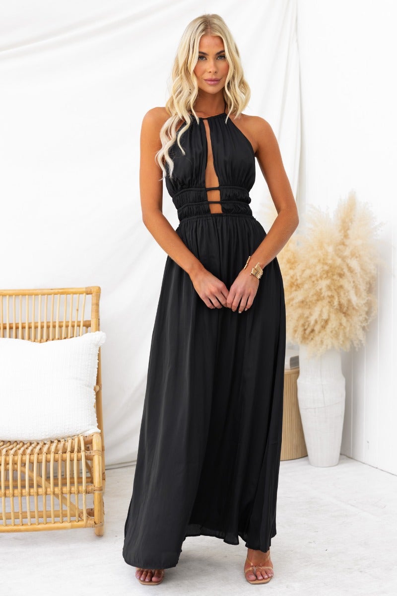 Black Kariah maxi dress with adjustable tie halter neckline, cut-outs, and elastic waistband, modeled in a stylish setting.