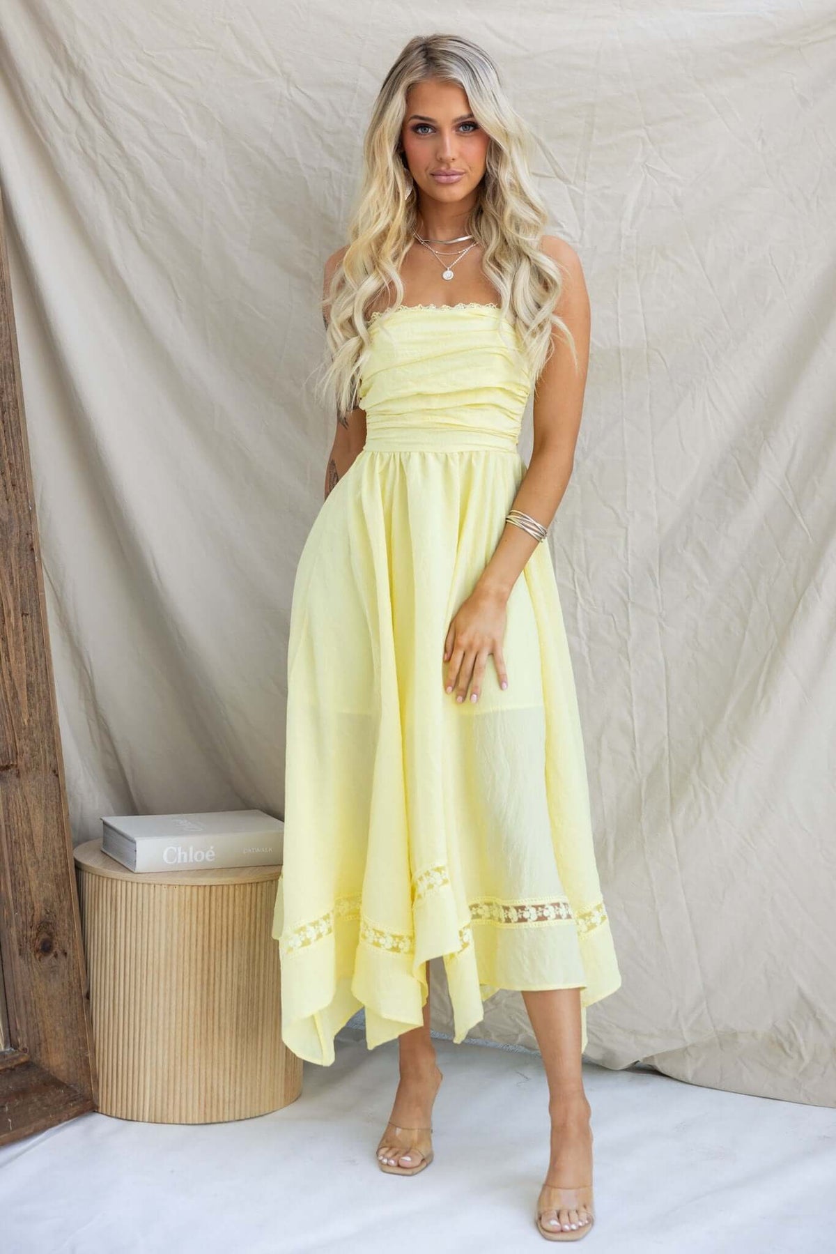 Civita Maxi Dress in yellow, strapless design with handkerchief hem, worn by a model in a stylish setting.