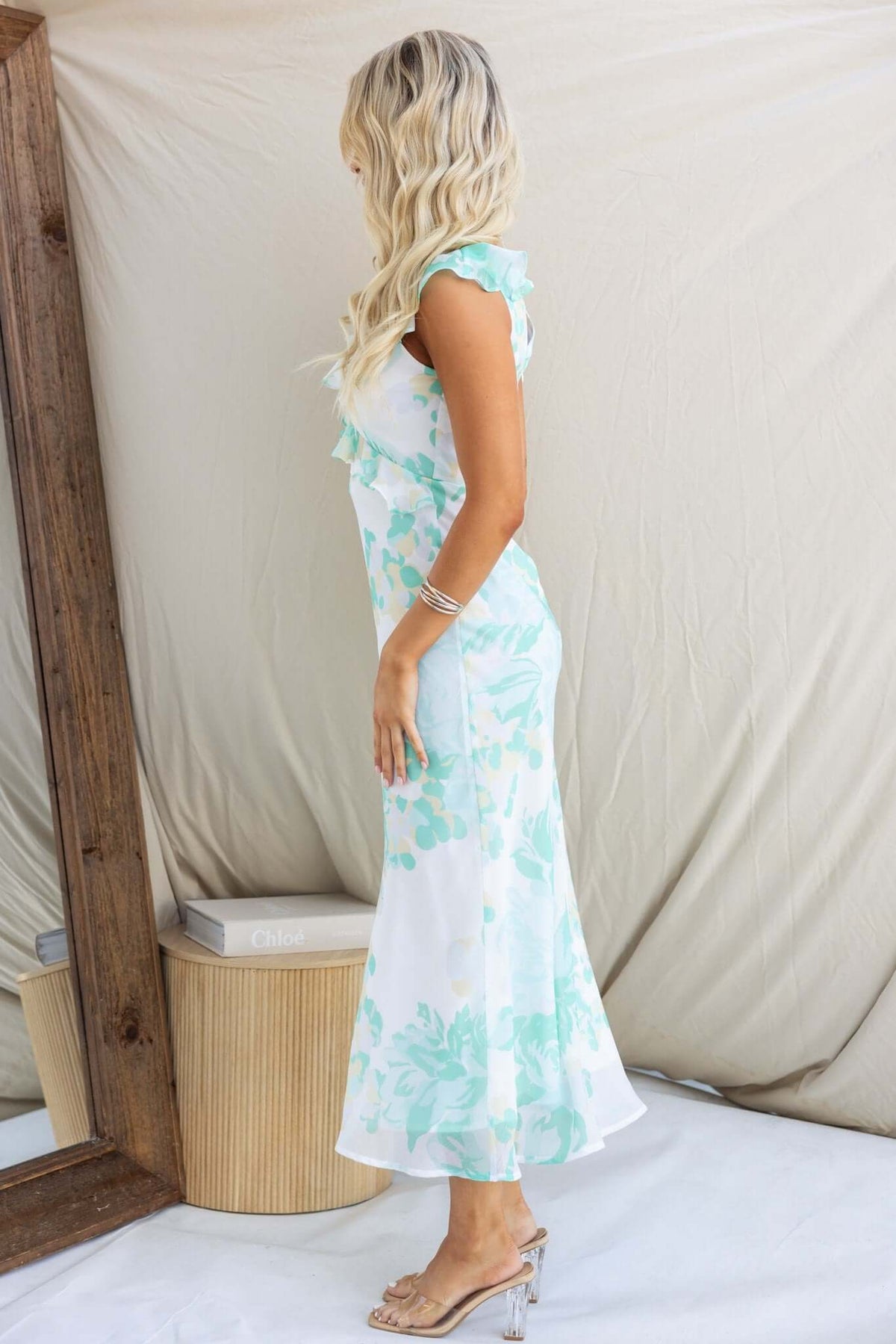 Side view of a woman in a Bonnet Maxi Dress with ruffle detail and floral pattern, styled with soft waves and minimal accessories.