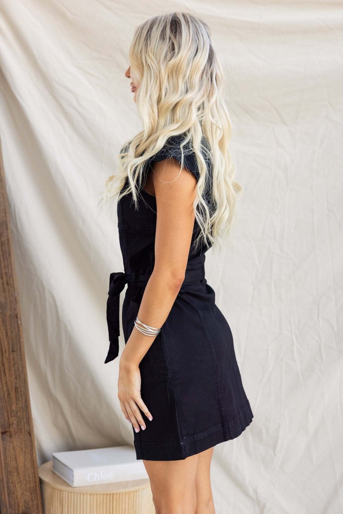 Side view of a woman wearing a black Forever Me Denim Dress, featuring a button-down front and removable belt.