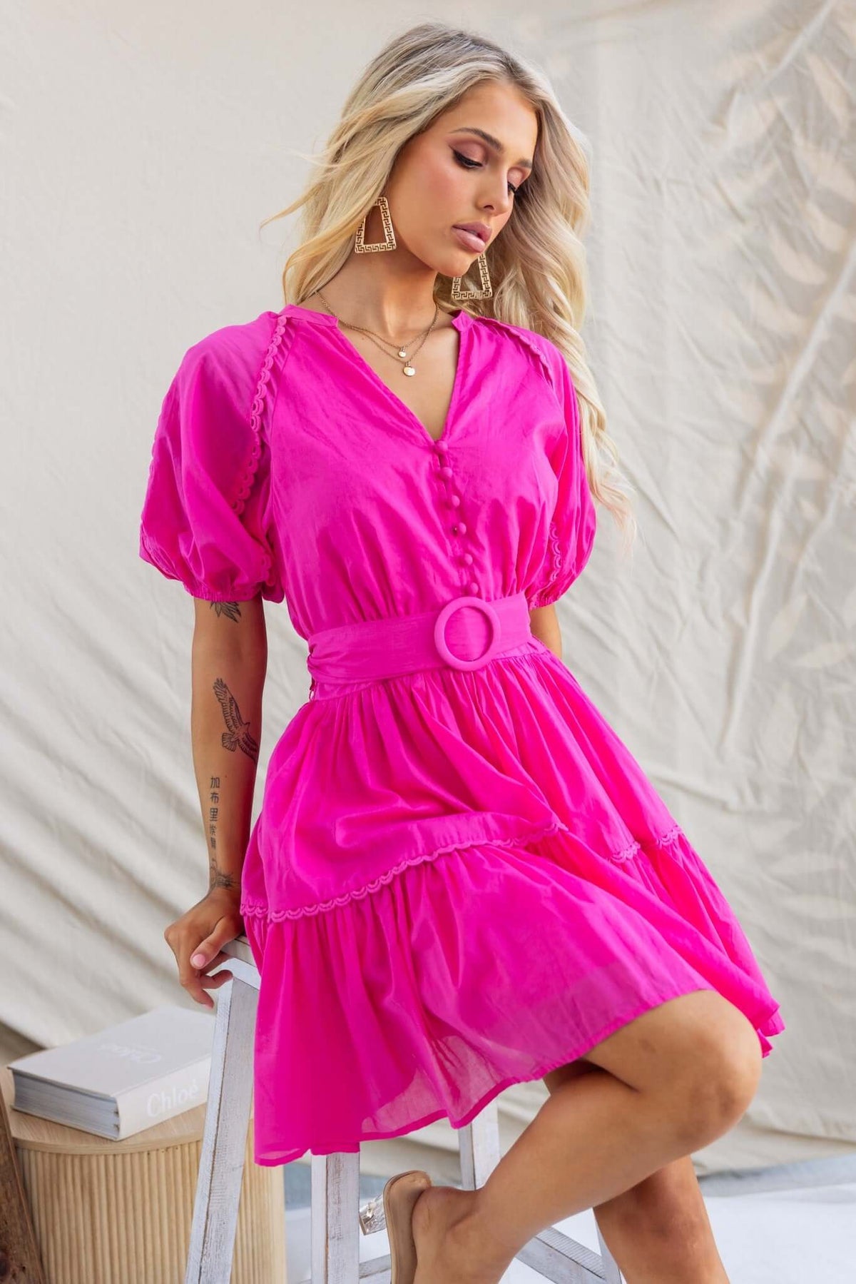 Model wearing a vibrant pink Verlaine Dress with a V-neckline, button-up detail, and removable tie, showcasing a stylish summer look.