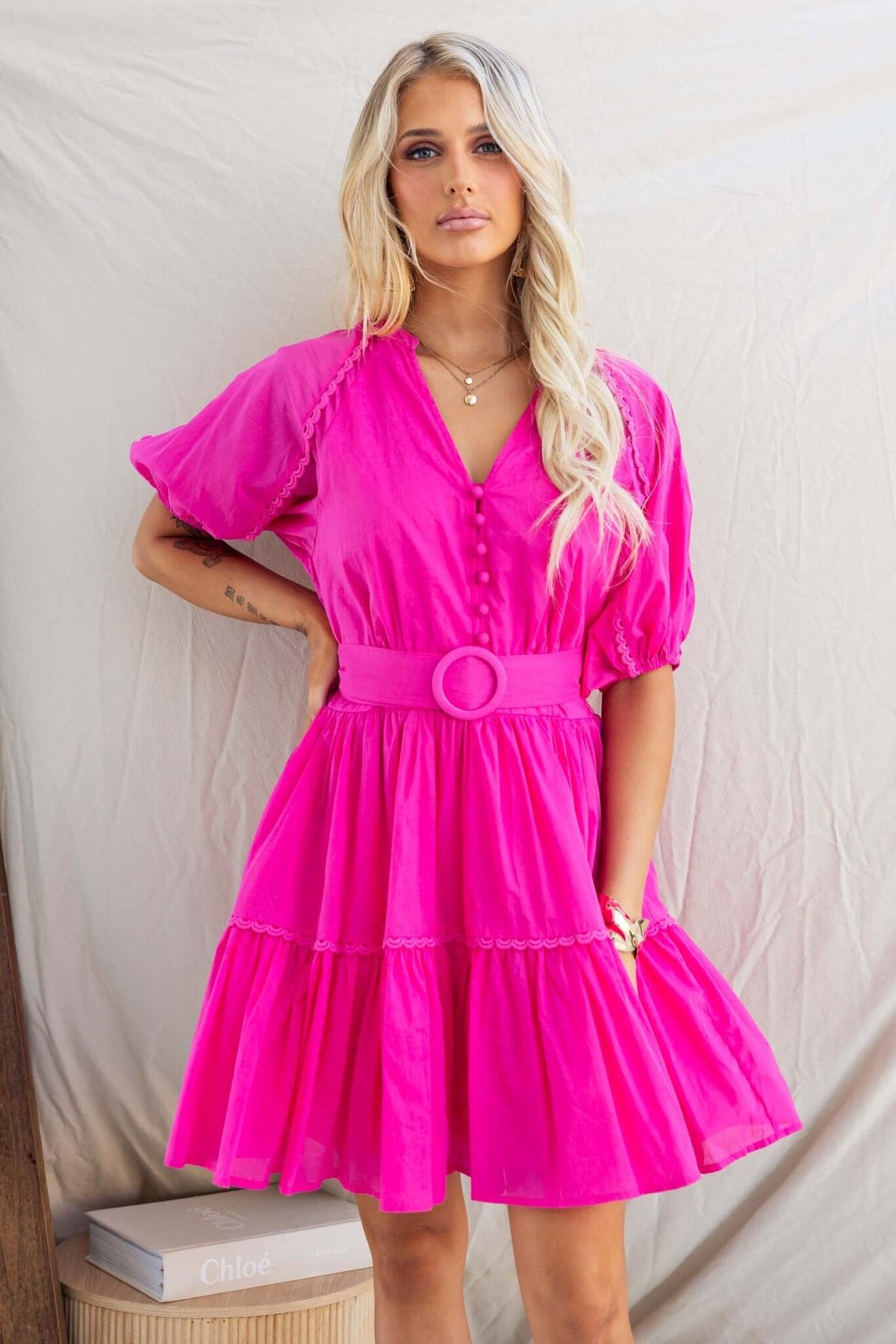 Verlaine Dress in vibrant pink, featuring V-neckline, button-up bust, elastic sleeves, removable tie, and pockets.