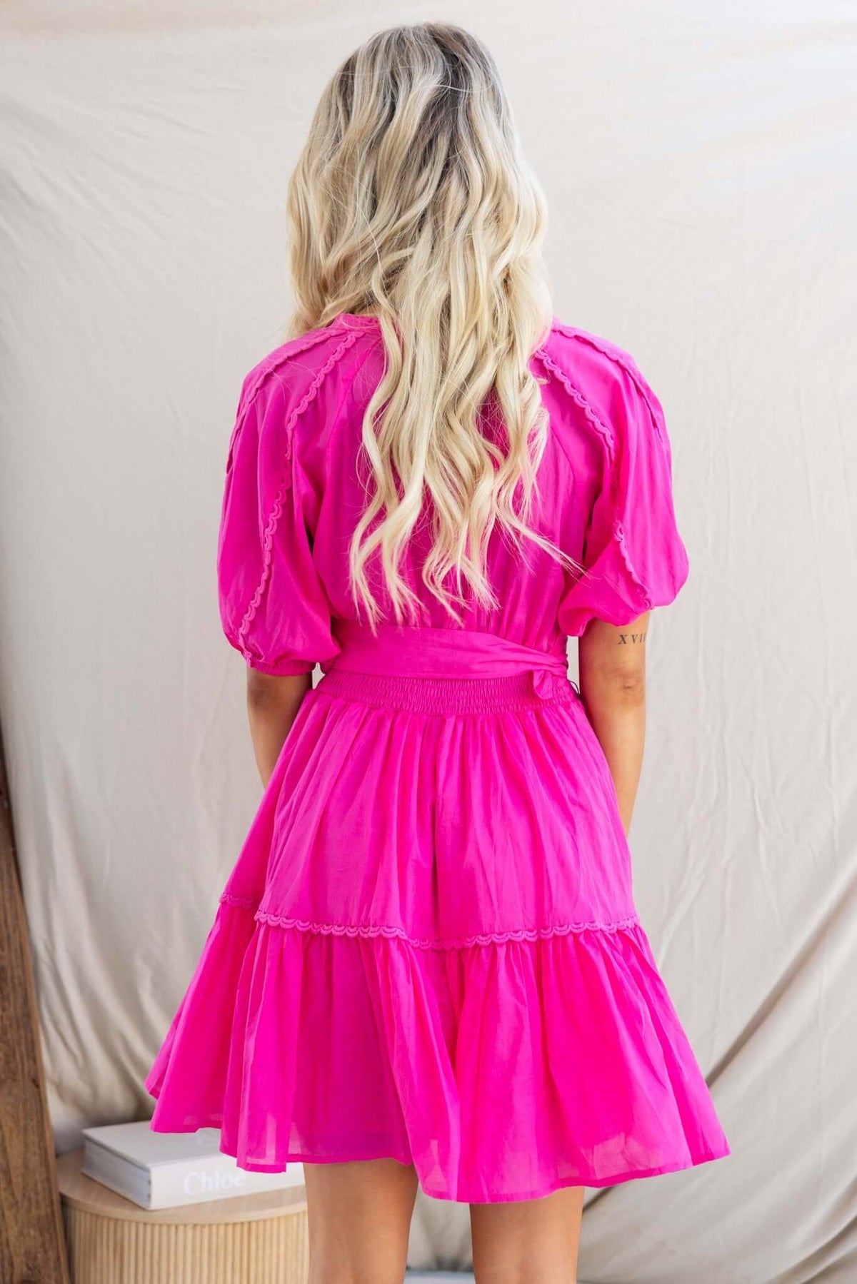 Back view of a model in a pink Verlaine dress featuring a tiered skirt and puff sleeves.