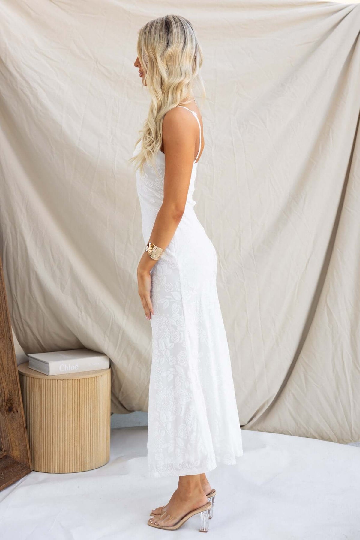 Side view of a woman wearing the Melita Maxi Dress in white, showcasing adjustable straps and embossed velvet print.