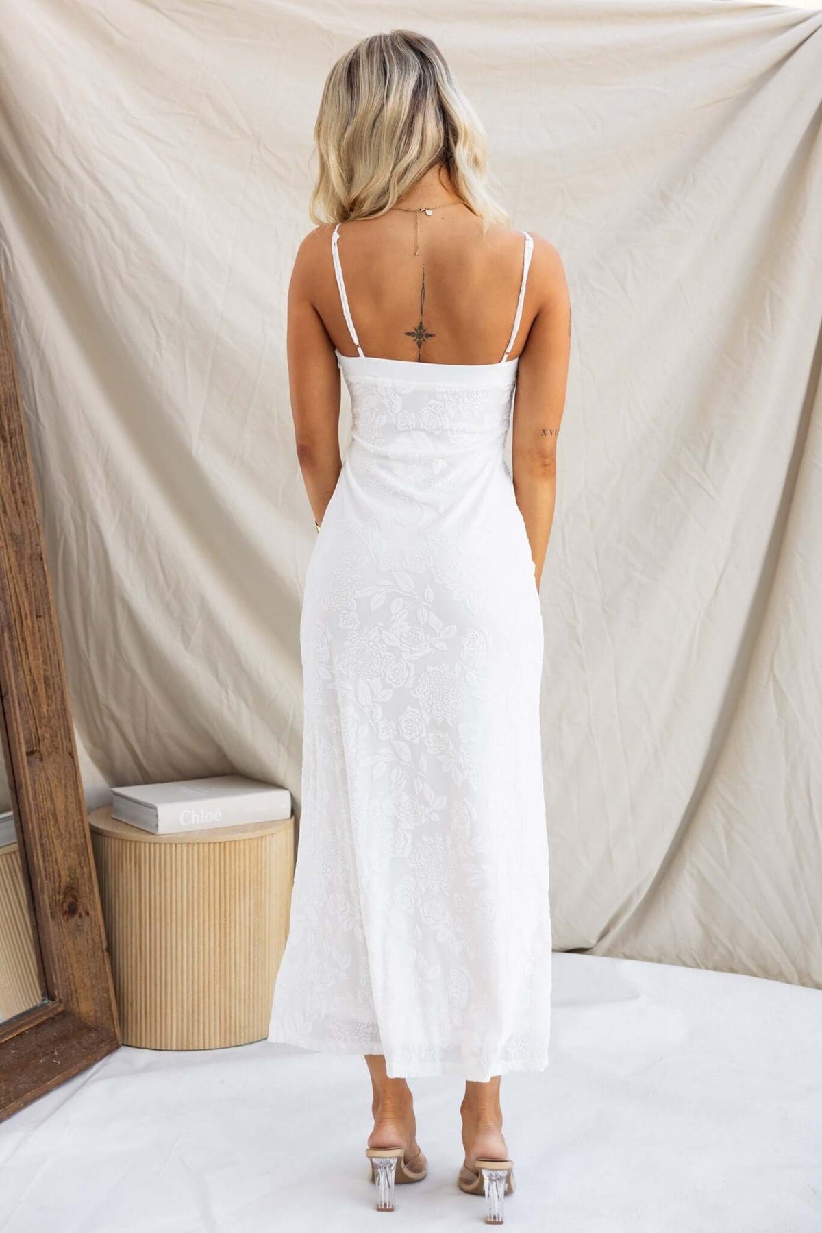 Back view of a woman in a white Melita Maxi Dress with adjustable straps and embossed velvet print, styled elegantly.