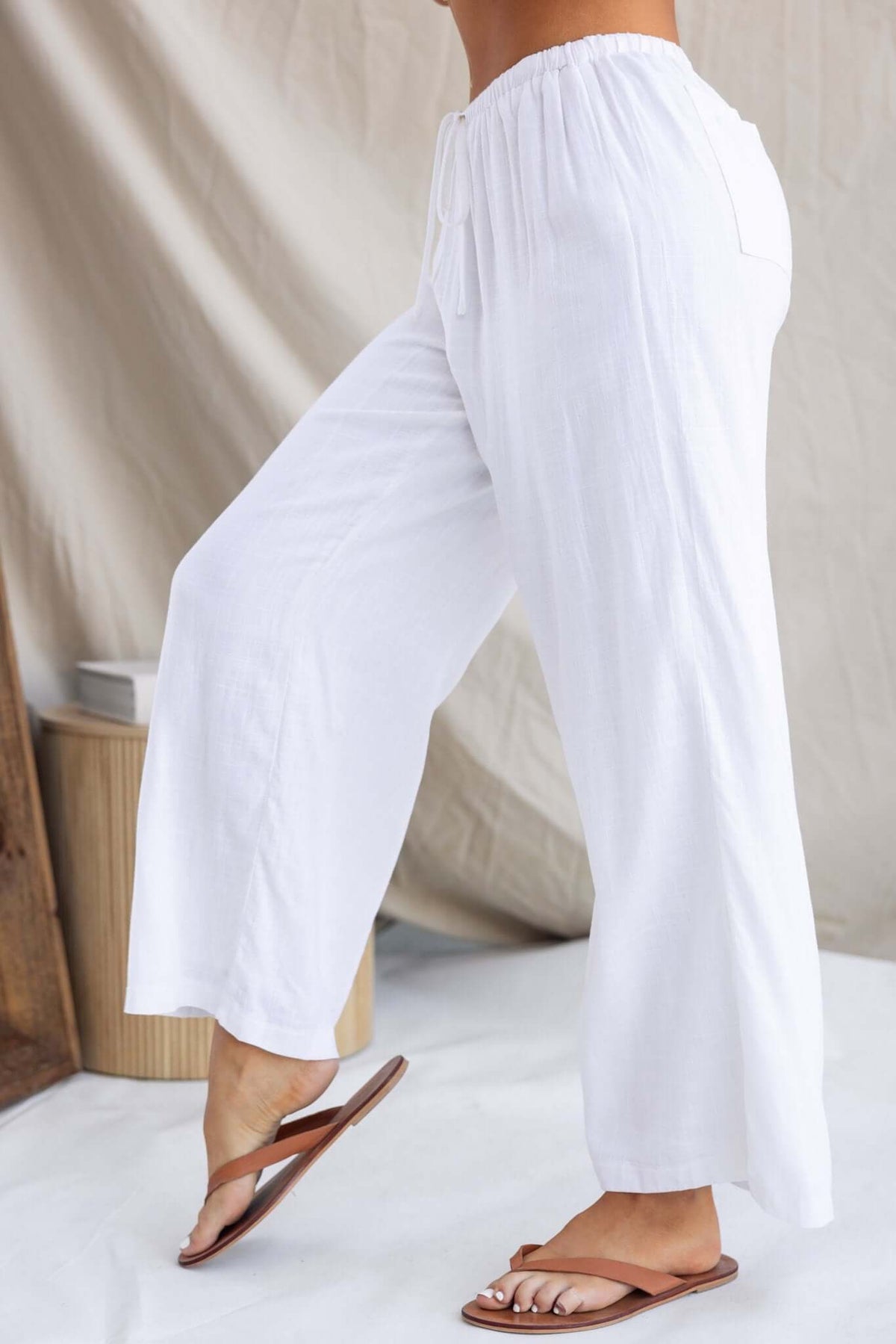 Irina Pants in white, featuring an elastic waistband, drawstring, and back pockets, styled with flip-flops.
