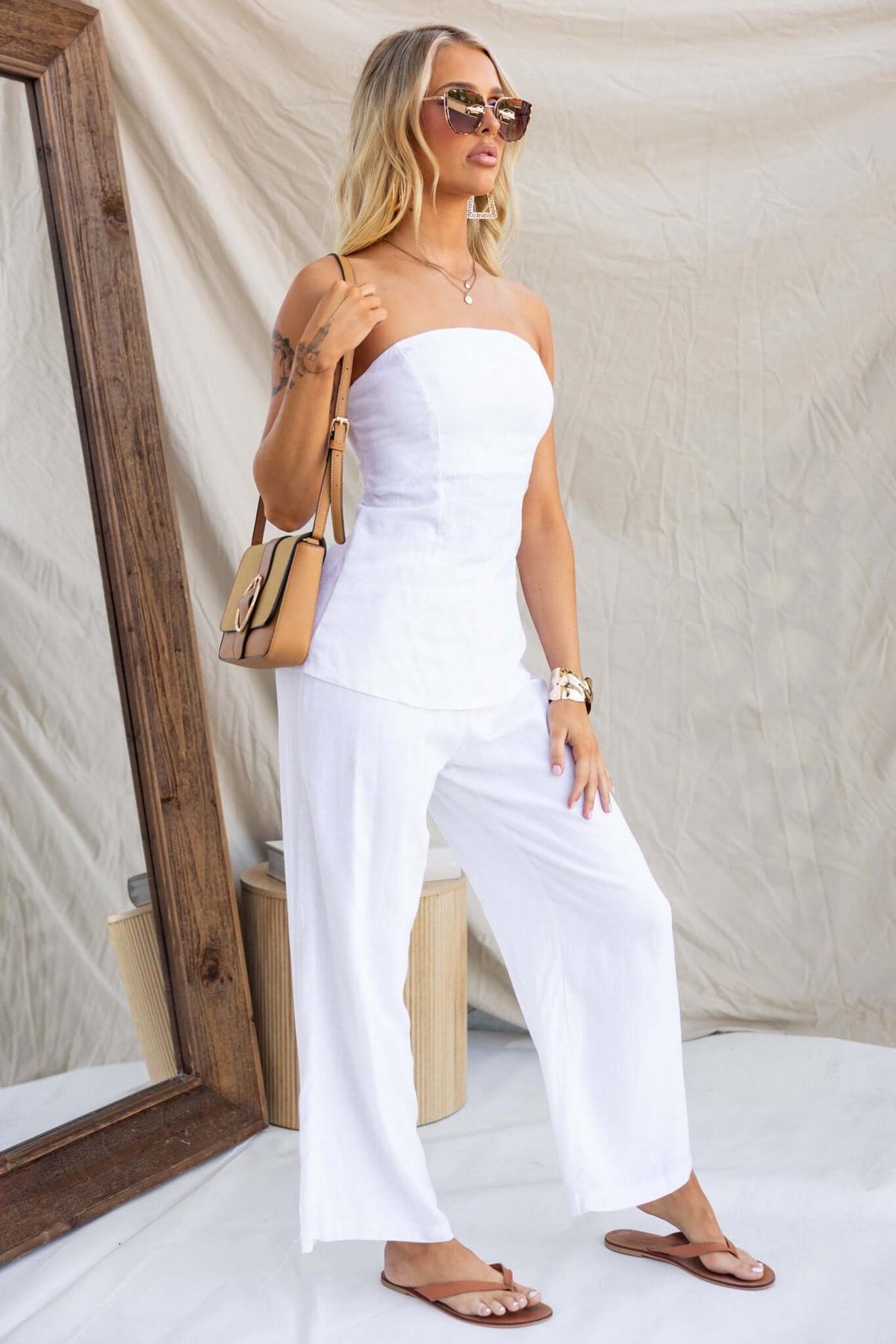 Model wearing Irina Pants with a strapless top and sunglasses, standing beside a large mirror in a white backdrop.
