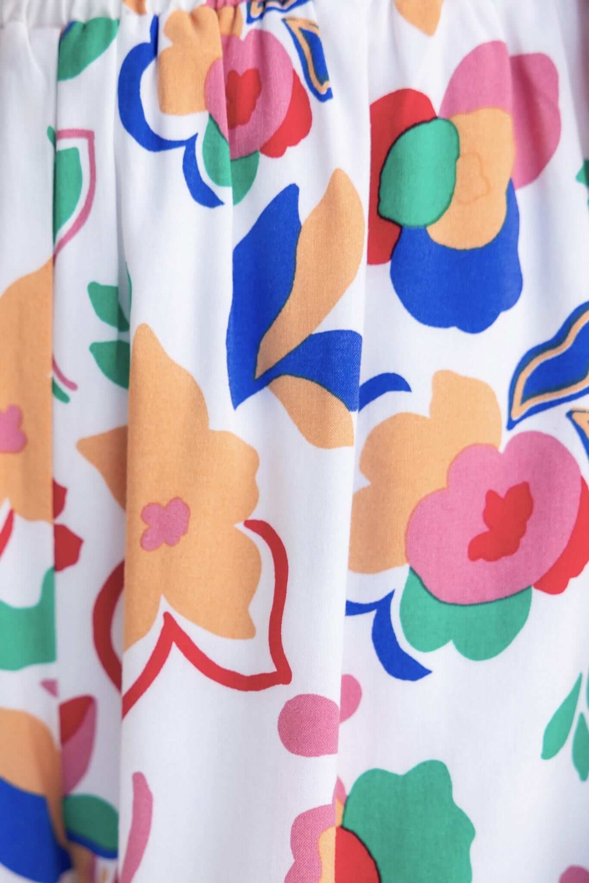 Colorful floral fabric pattern featuring vibrant flowers in shades of pink, blue, green, and orange on a white background.