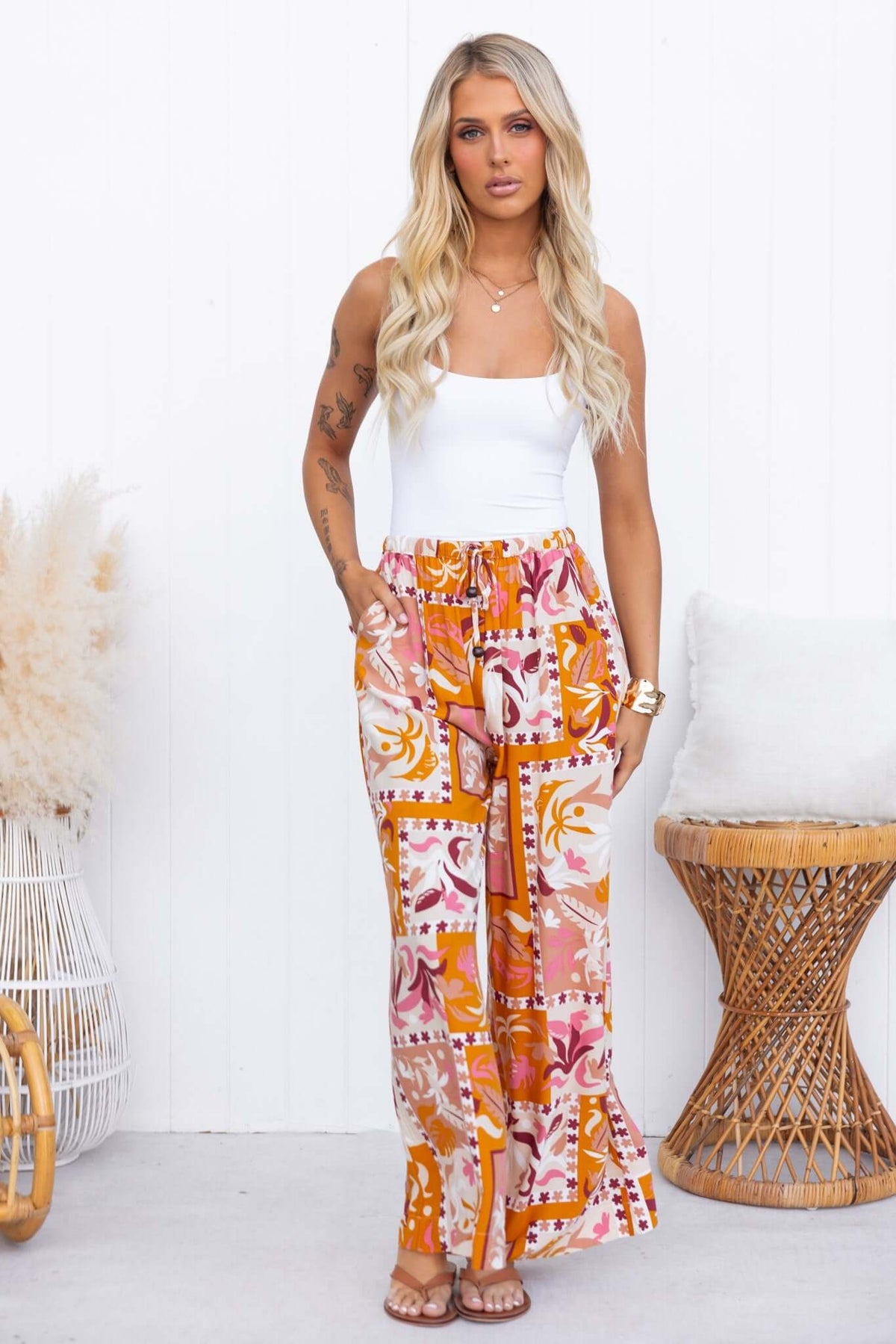 Model showcasing Valora Pants, mid-high waist, elastic waistband, vibrant floral print, styled with a basic tank top.
