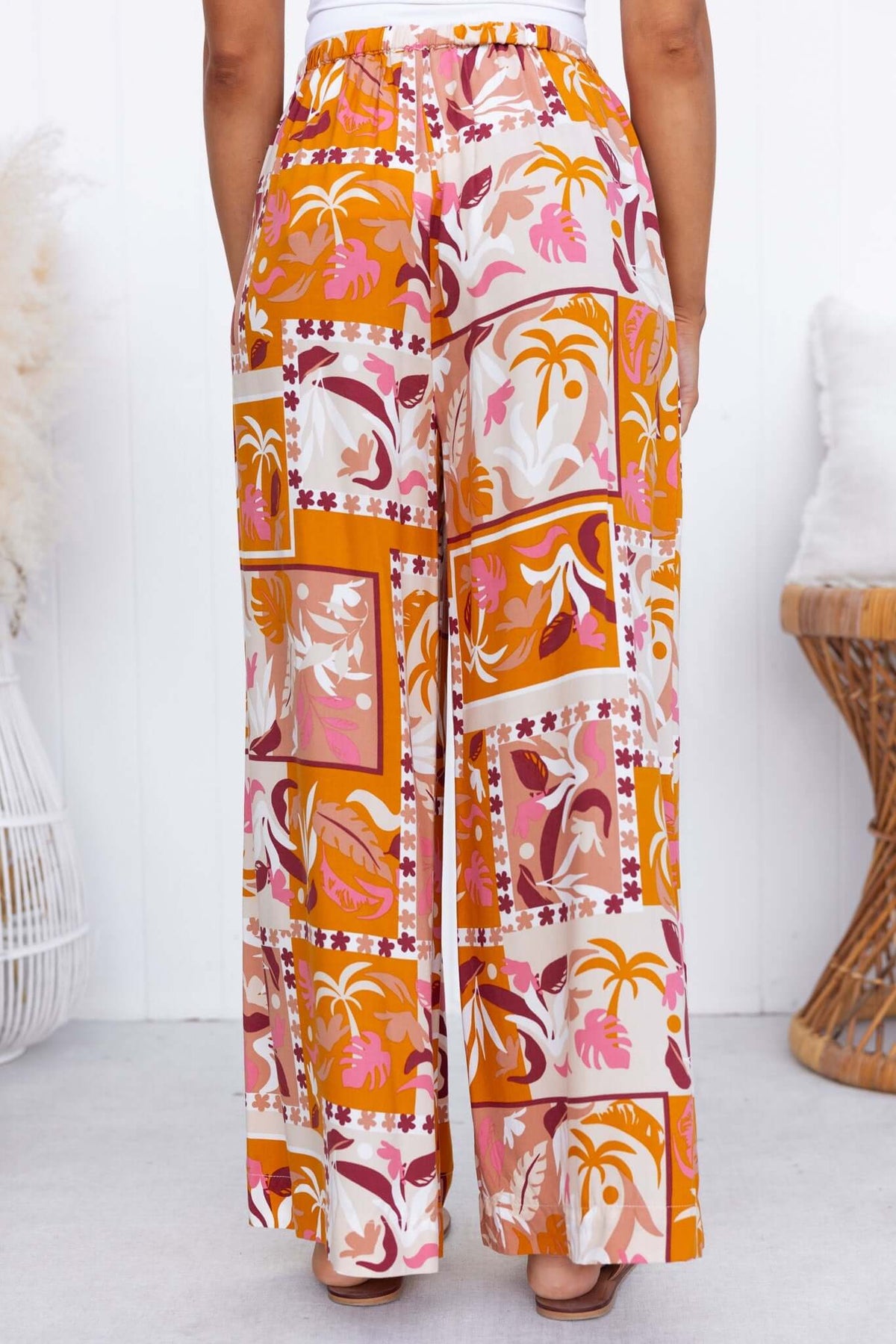 Valora Pants featuring a mid-high waist, elastic waistband, pockets, and vibrant floral patterns in warm colors.