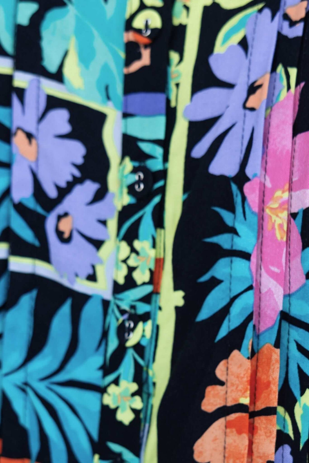 Close-up of Delray Top featuring vibrant floral print and adjustable button-up front in black background.