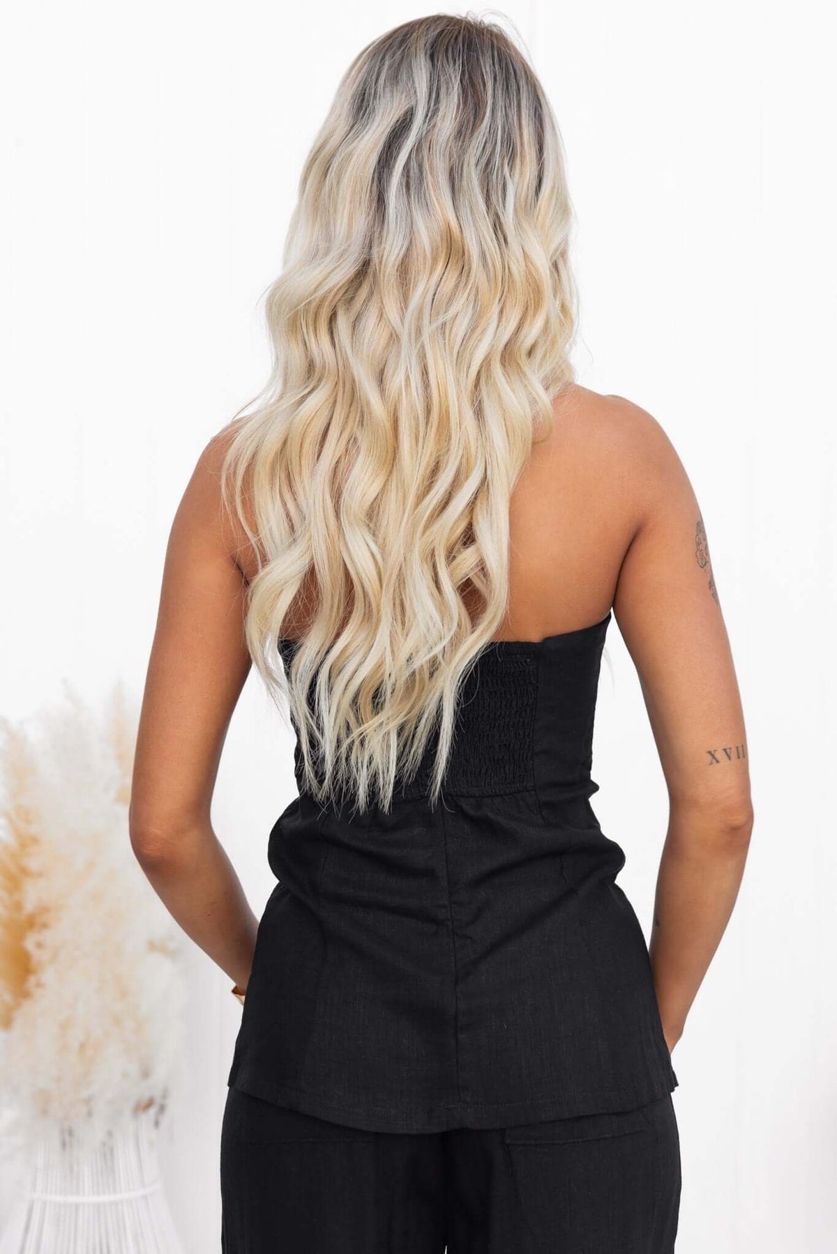 Back view of a model wearing a black strapless Irina top with a linen texture and elastic back.