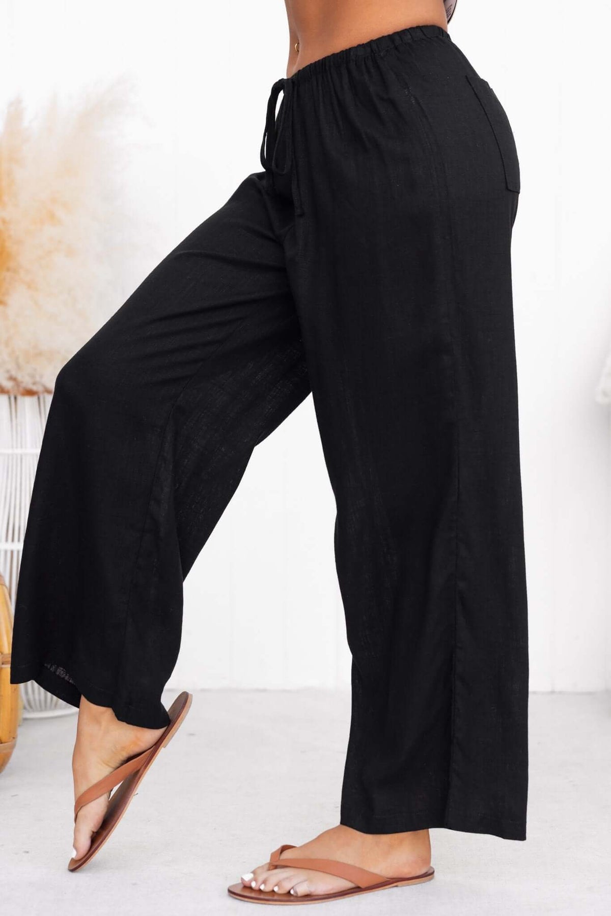 Irina Pants in black with elastic waistband, drawstring, and back pockets, styled with flip-flops.