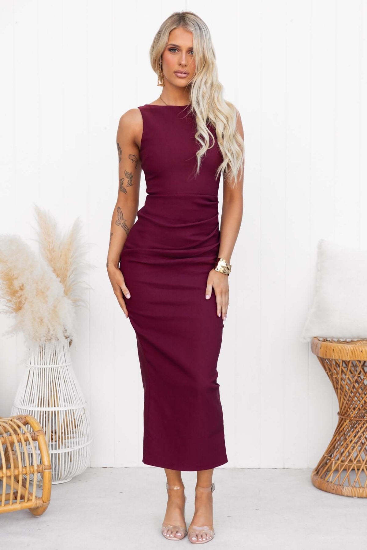 Elegant burgundy Maris Maxi Dress with high neckline and back split, styled with clear heels and boho decor.