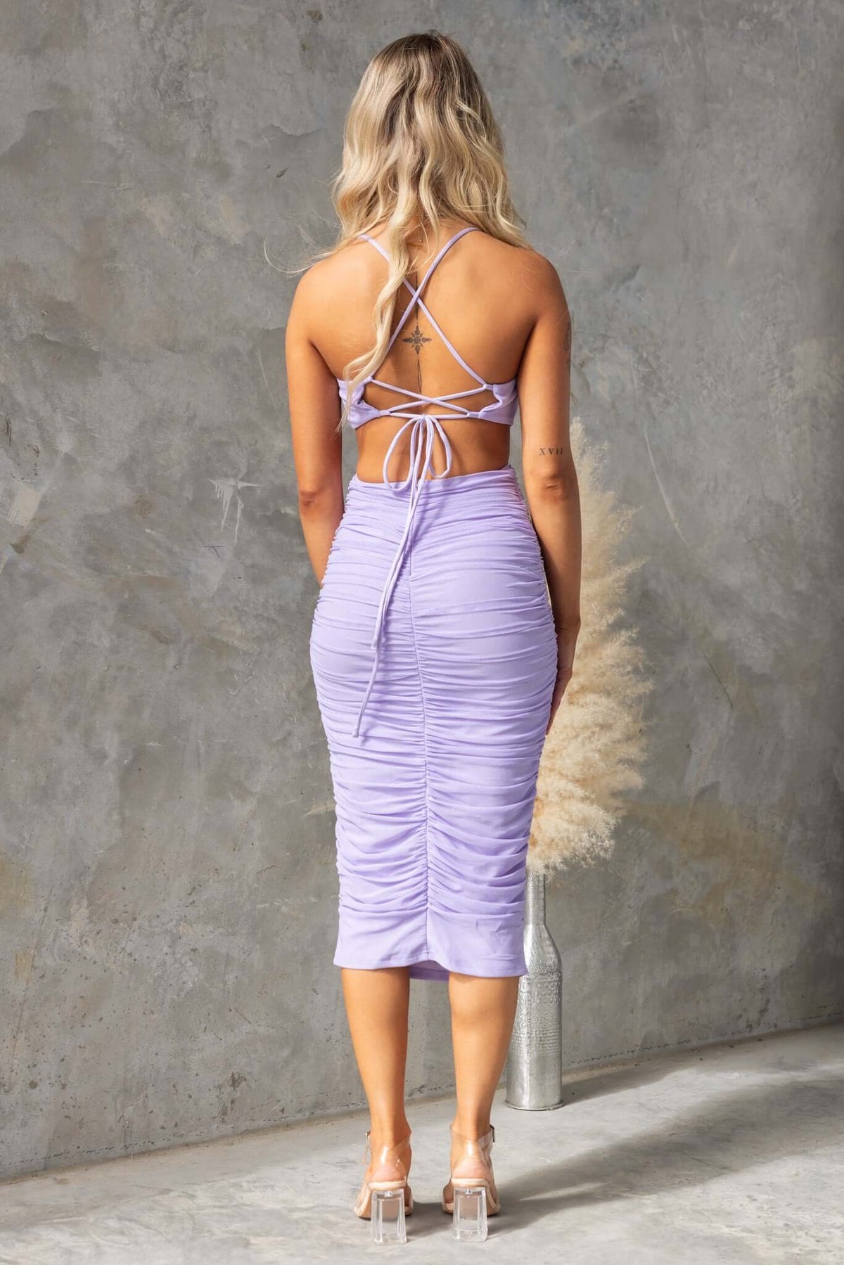 Woman wearing a lilac midi dress with adjustable tie straps and ruching, showcasing a cut-out design at the waist.