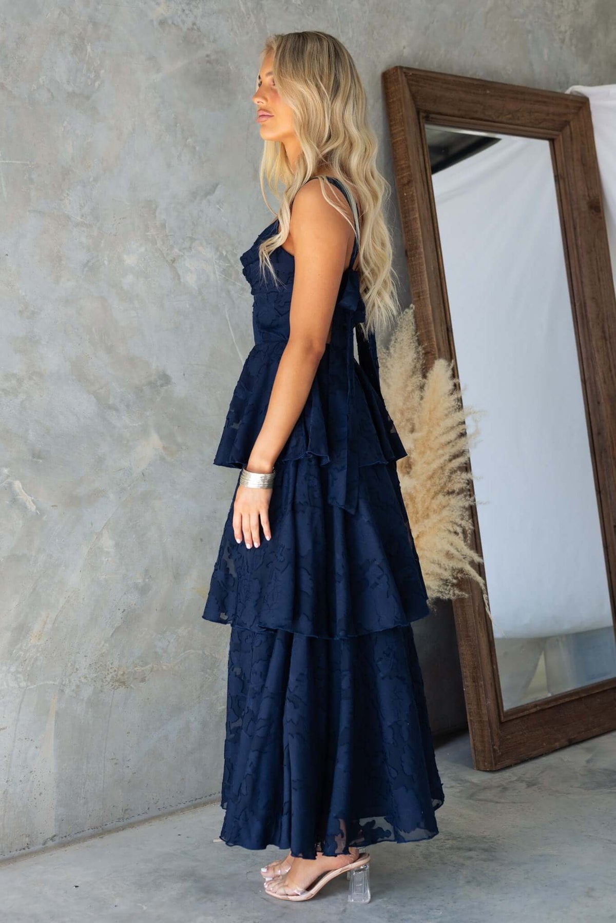 Model wearing a navy Rivoli Maxi Dress with tie straps and ruffle skirt, styled against a minimalist backdrop.
