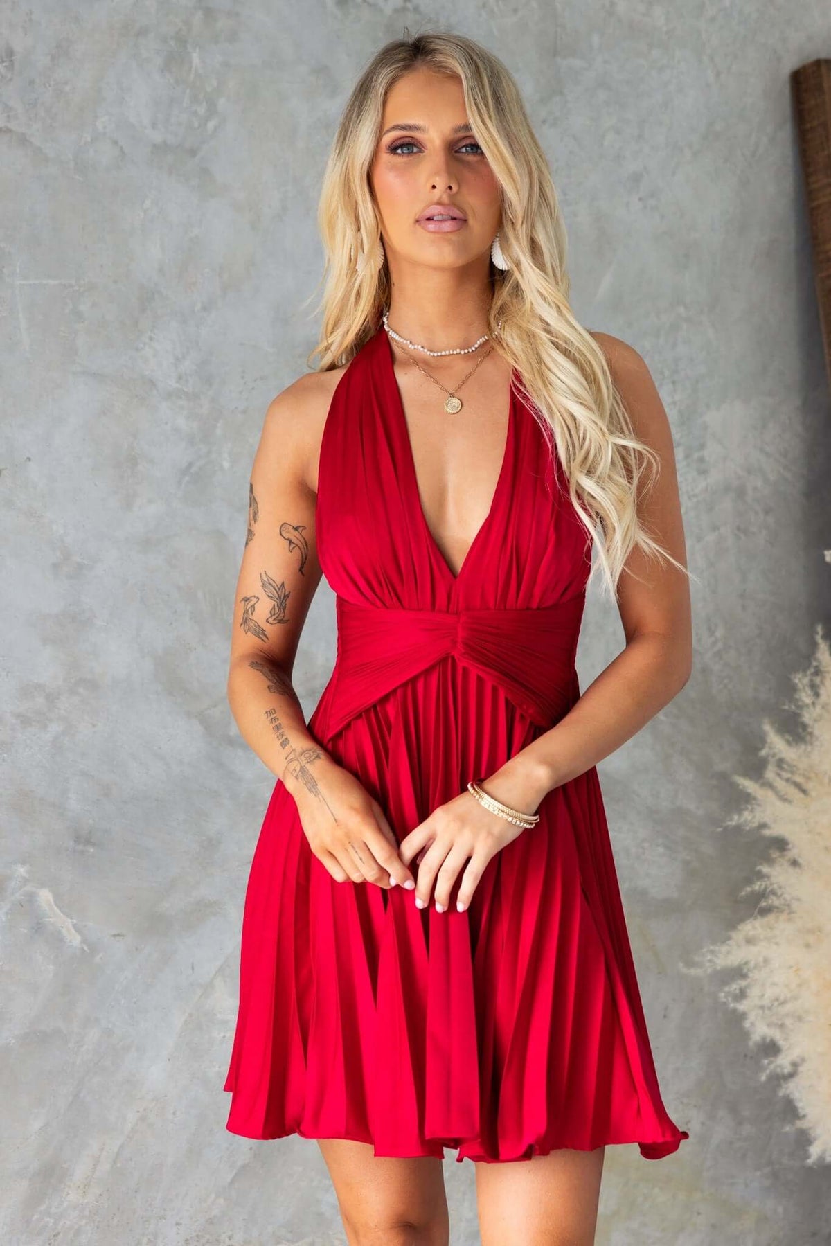 Model wearing a red special day dress with adjustable neckline and pleated skirt, set against a textured backdrop.