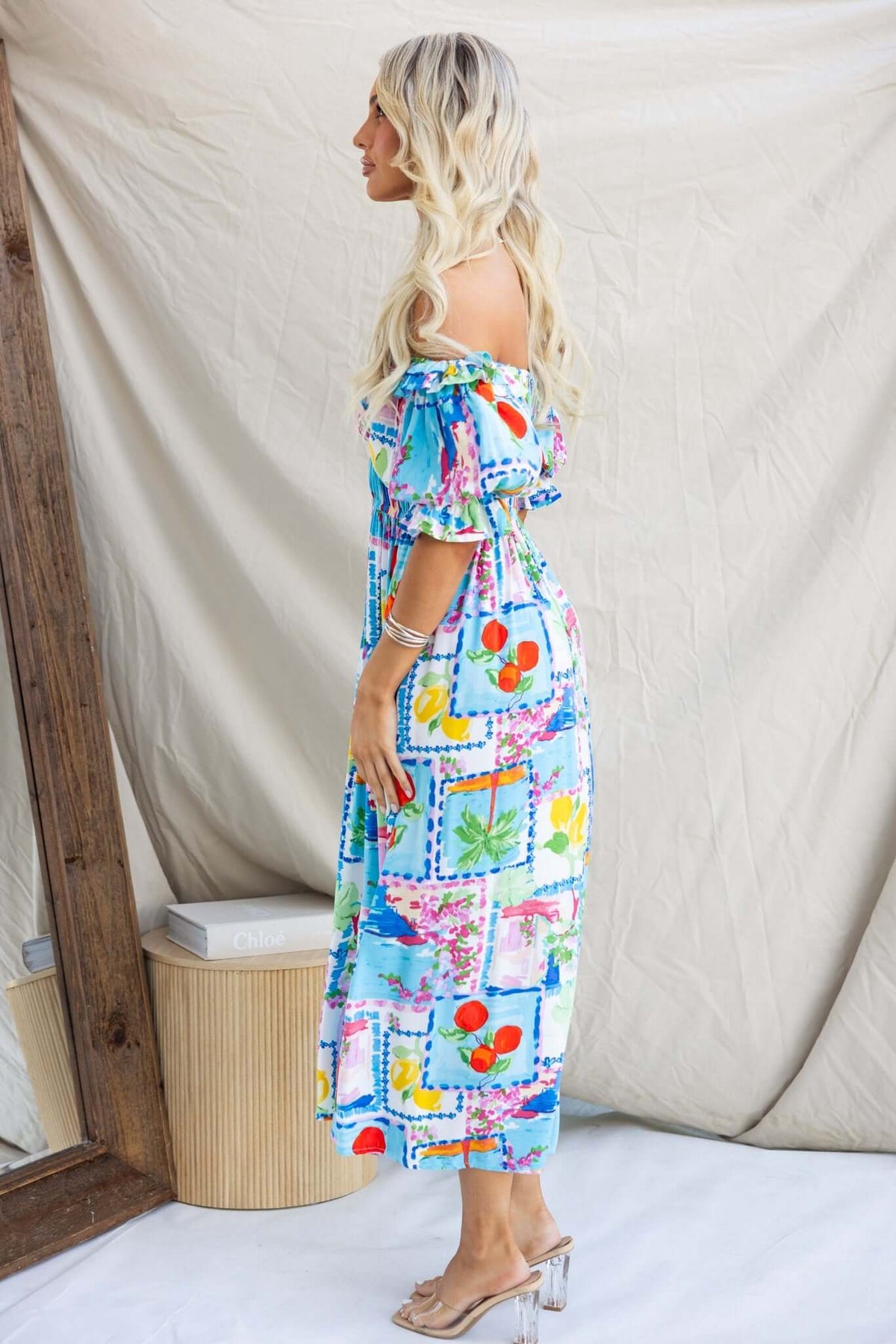 Side view of a woman wearing a colorful Dewberry Maxi Dress with off-shoulder neckline and pockets.