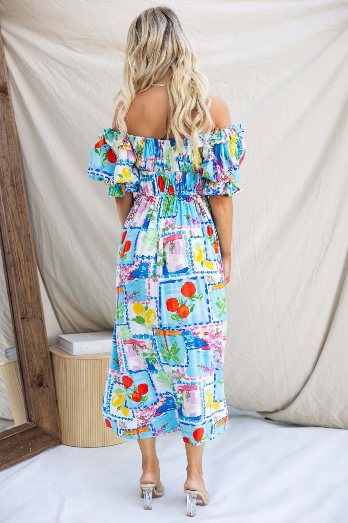 Back view of a woman in a colorful off-shoulder Dewberry maxi dress with ruffled sleeves and pockets.