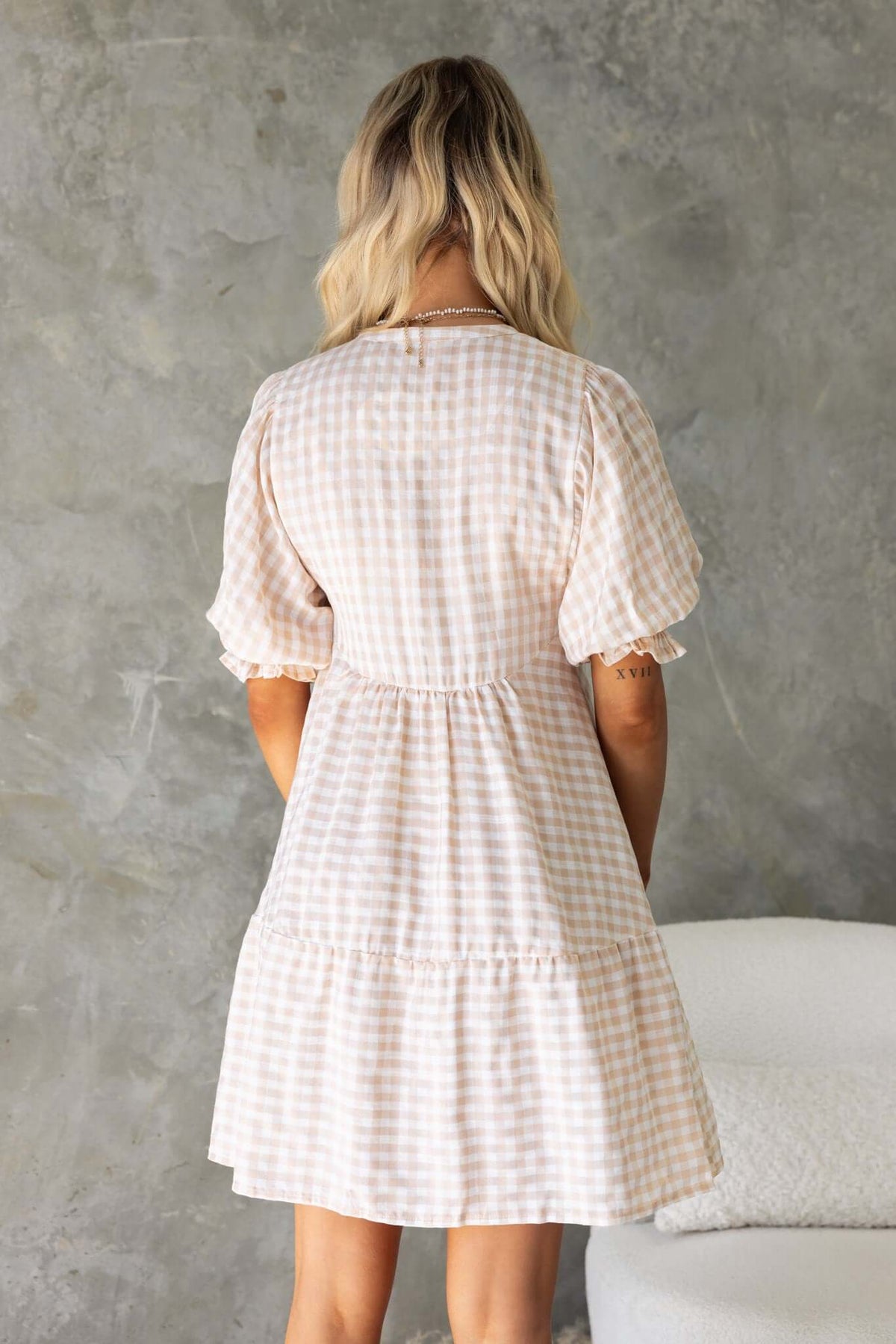 Back view of the Swinton Dress featuring a tie neckline and elastic sleeves in a checkered pattern.