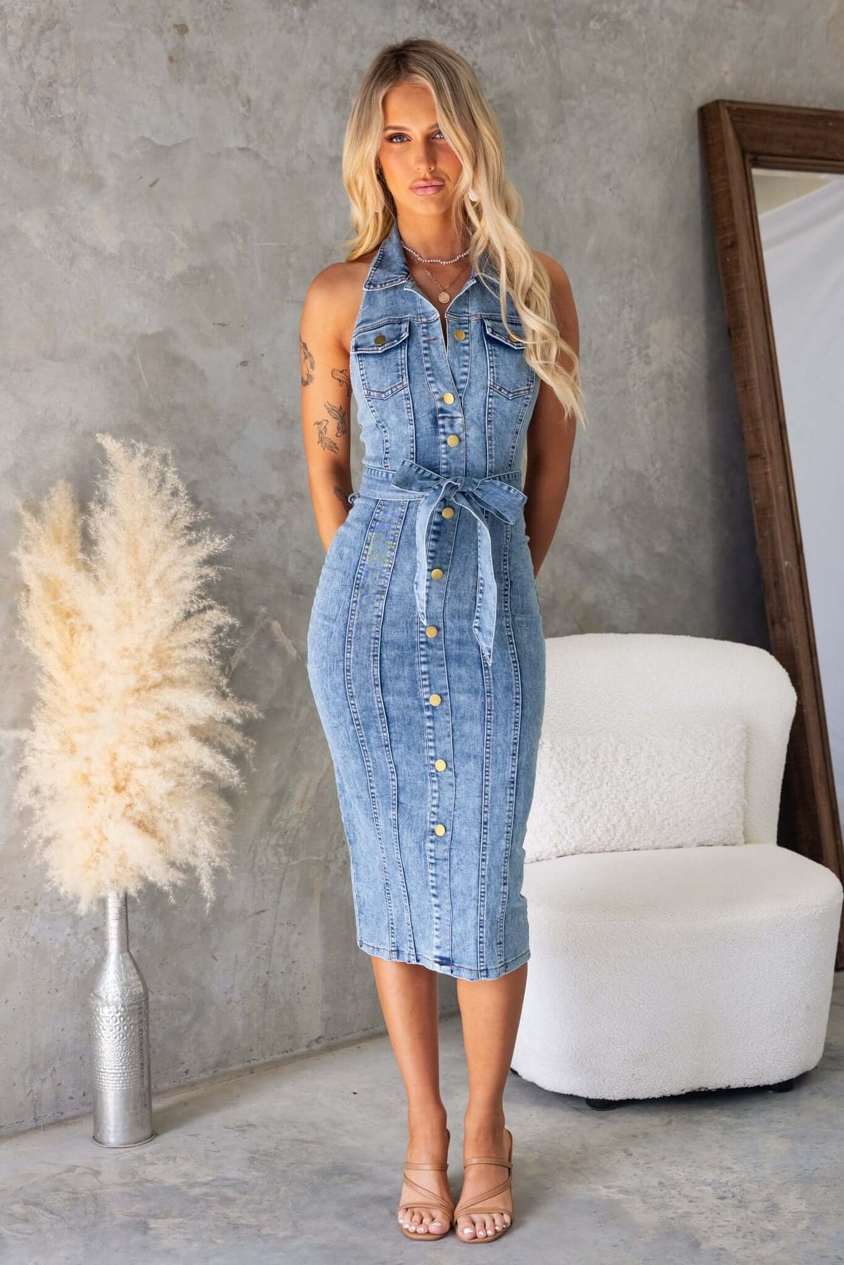Model wearing Kalyn Denim Midi Dress featuring a high neckline, pockets, and removable tie, set against a stylish backdrop.