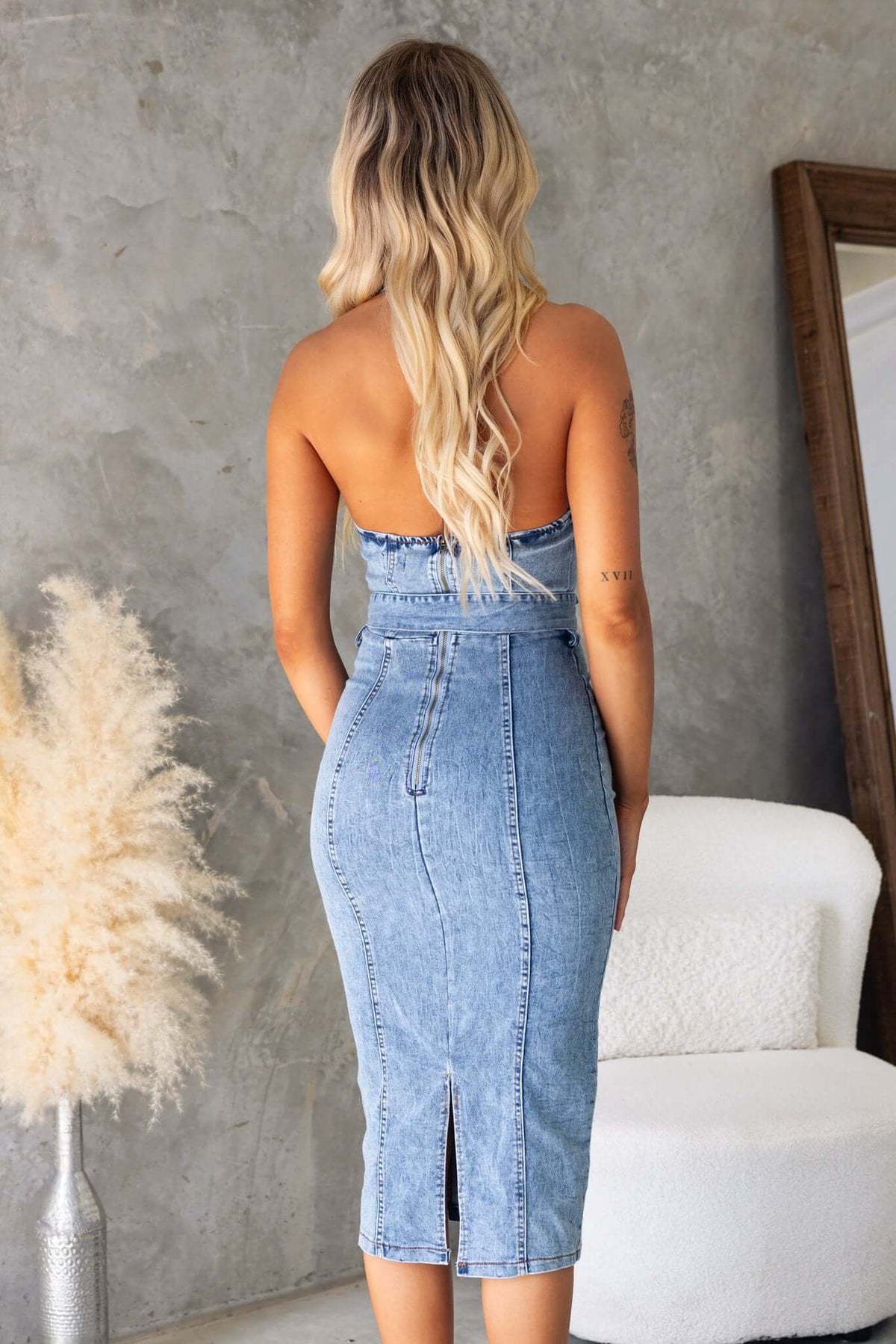 Back view of a woman in a Kalyn Denim Midi Dress, showcasing its fitted design and stylish split.