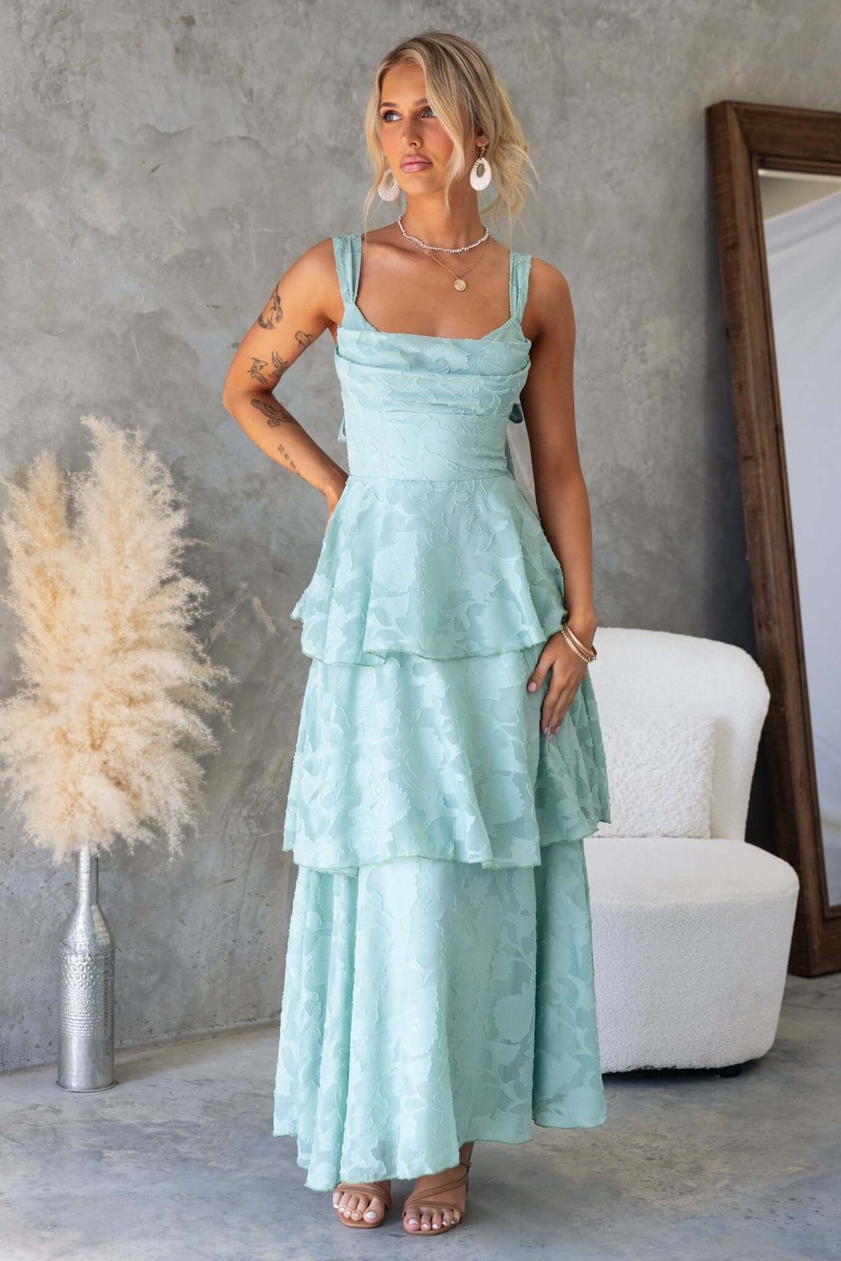 Model wearing a light blue Rivoli Maxi Dress with a cowl neckline and layered ruffle skirt in a stylish indoor setting.