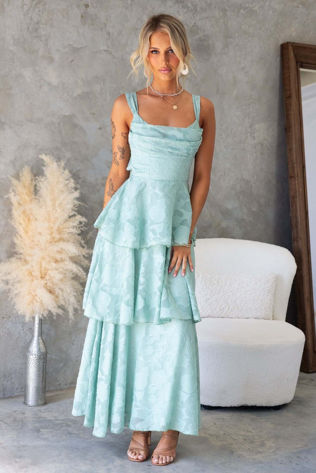 Rivoli Maxi Dress in mint green with a cowl neckline, tie straps, and ruffle skirt, styled in a modern interior.