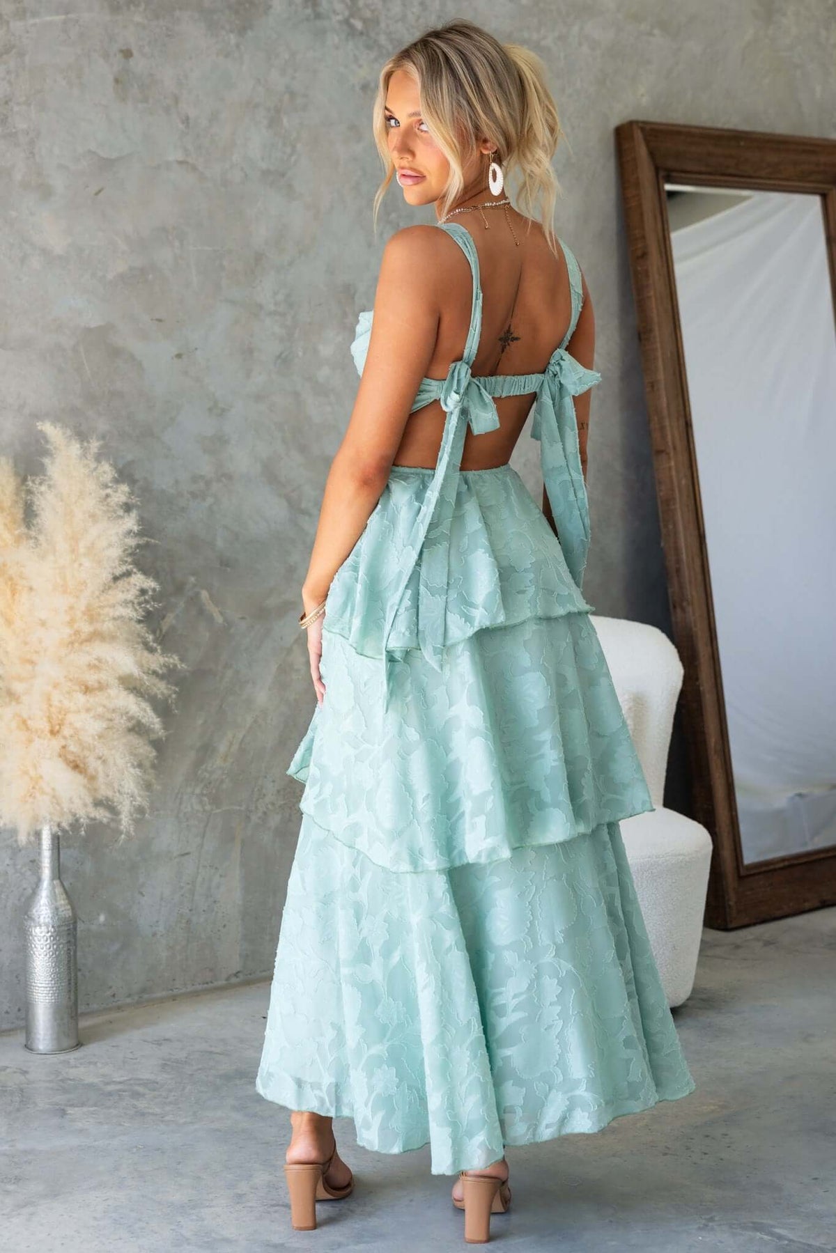 Back view of a model wearing a mint green Rivoli Maxi Dress with tie straps and a layered ruffle skirt.