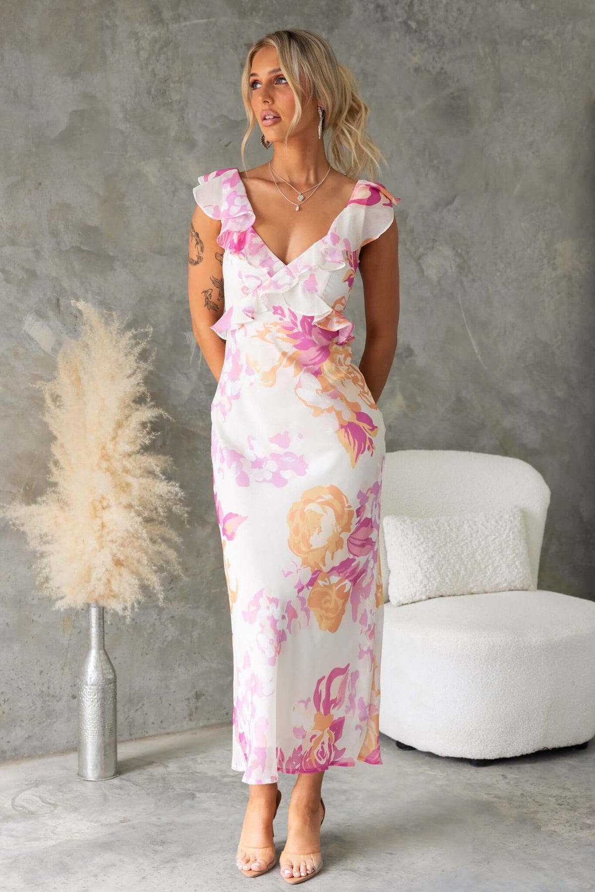 Model wearing a Bonnet Maxi Dress with floral design, featuring a V-neckline and ruffle detail against a textured background.