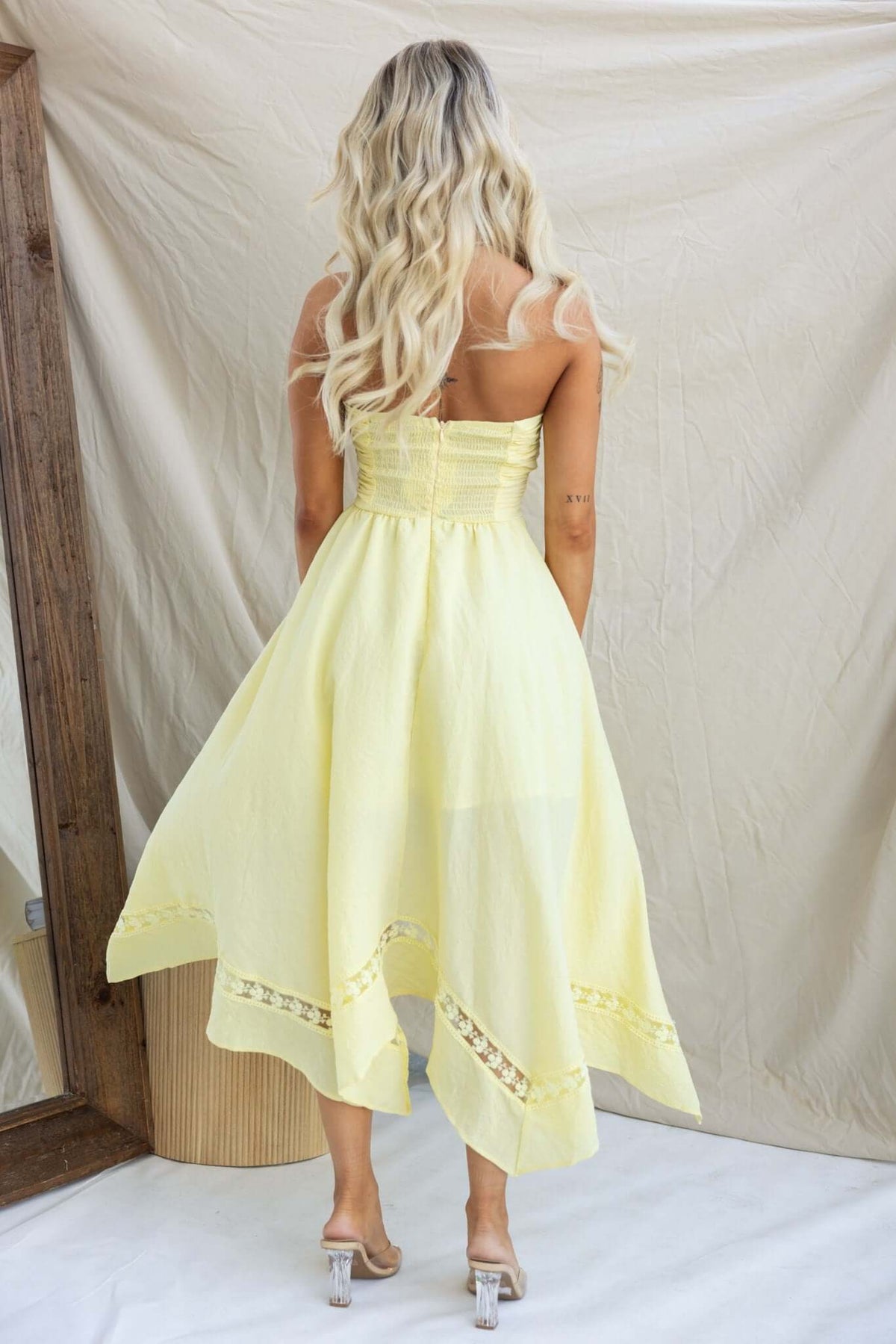 Model wearing a yellow strapless Civita maxi dress with a handkerchief hem seen from the back.