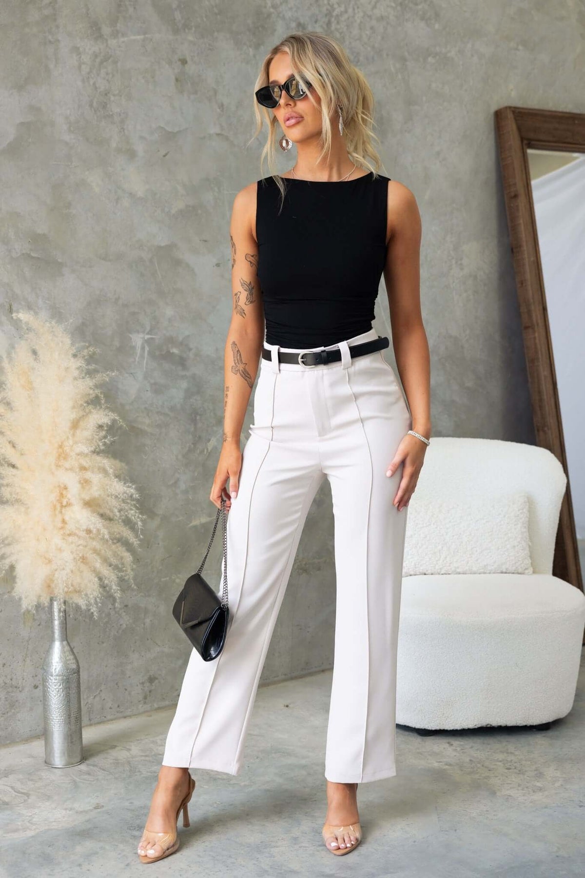 Model wearing a black cotton blend top with a boat neckline and white high-waisted pants against a neutral backdrop.