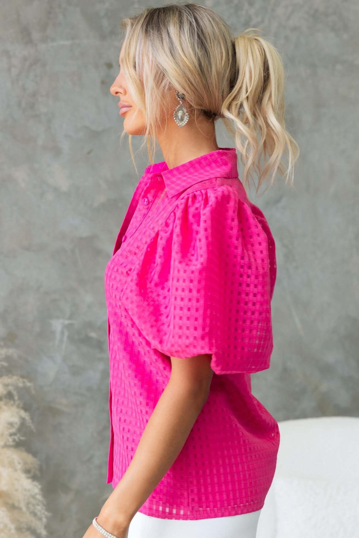 Profile view of a woman in a vibrant pink Ursa Shirt with puff sleeves and a button-up front.