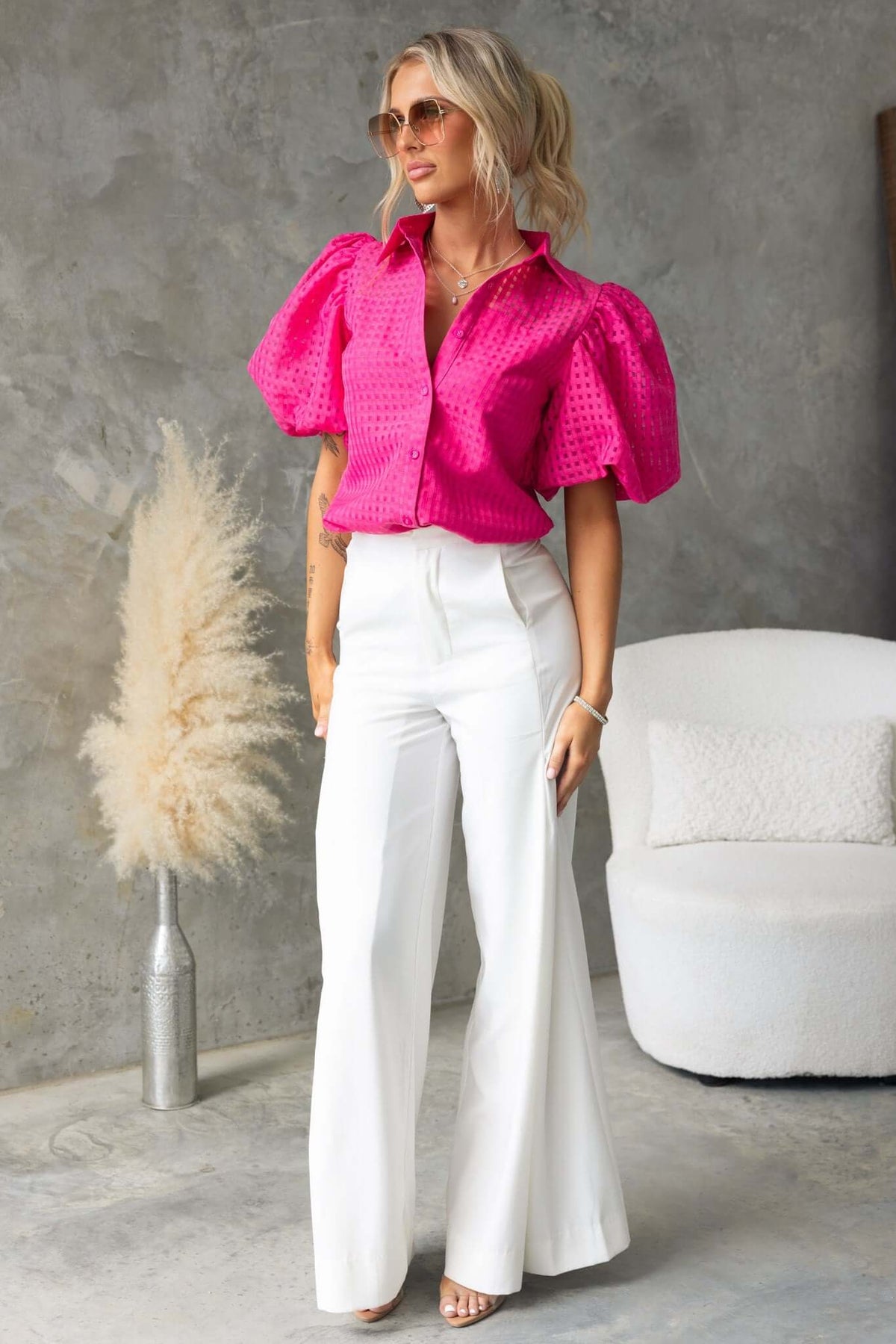 Model wearing a pink Ursa Shirt with puff sleeves, styled with white wide-leg pants in a minimalist setting.