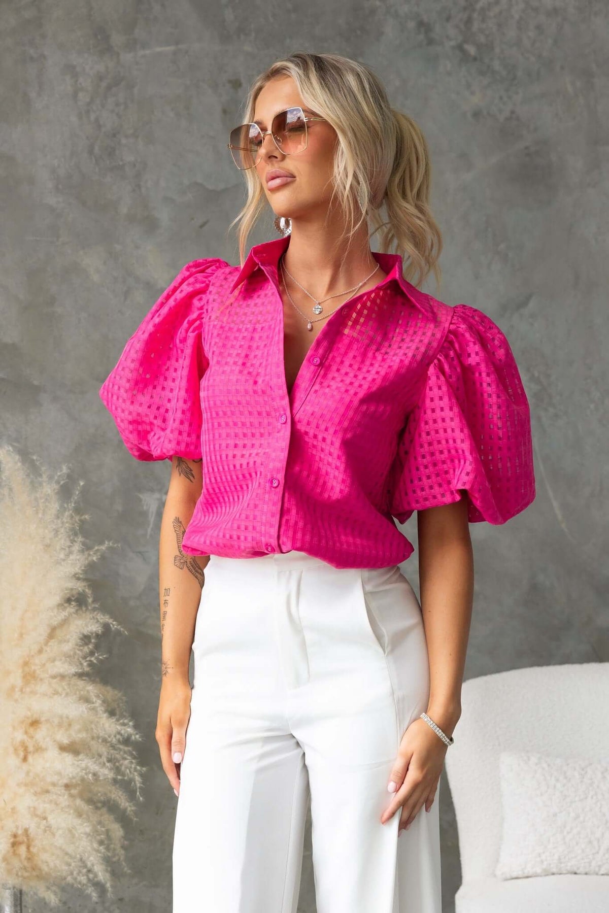 Model wearing Ursa Shirt, a pink button-up blouse with puff sleeves, styled with white pants and sunglasses.