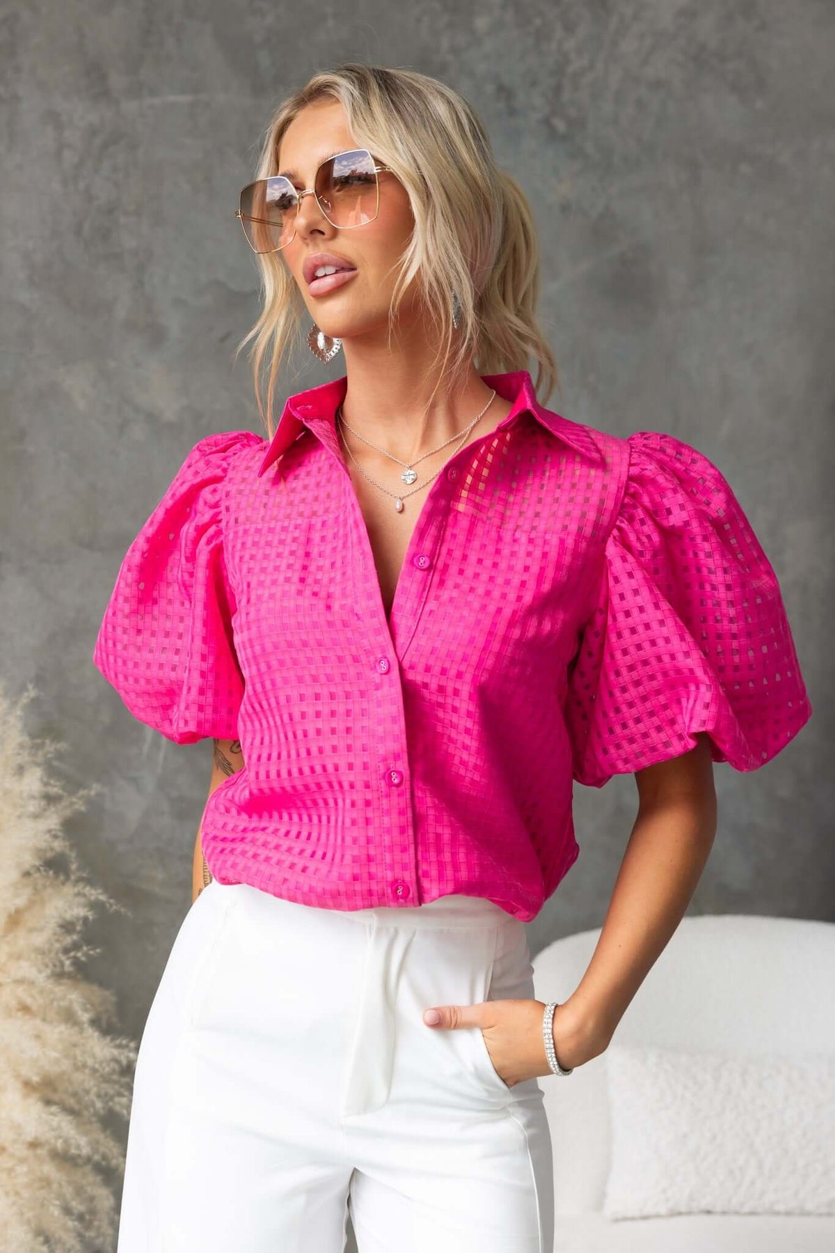 Stylish woman wearing pink Ursa Shirt with collar and puff sleeves, paired with white pants and sunglasses.