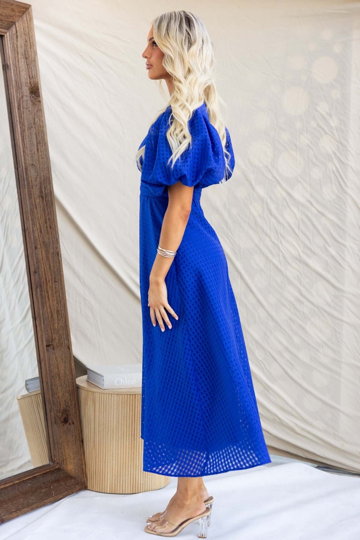 Side view of a woman wearing a blue Nosita midi dress with puff sleeves and textured detail in a stylish setting.