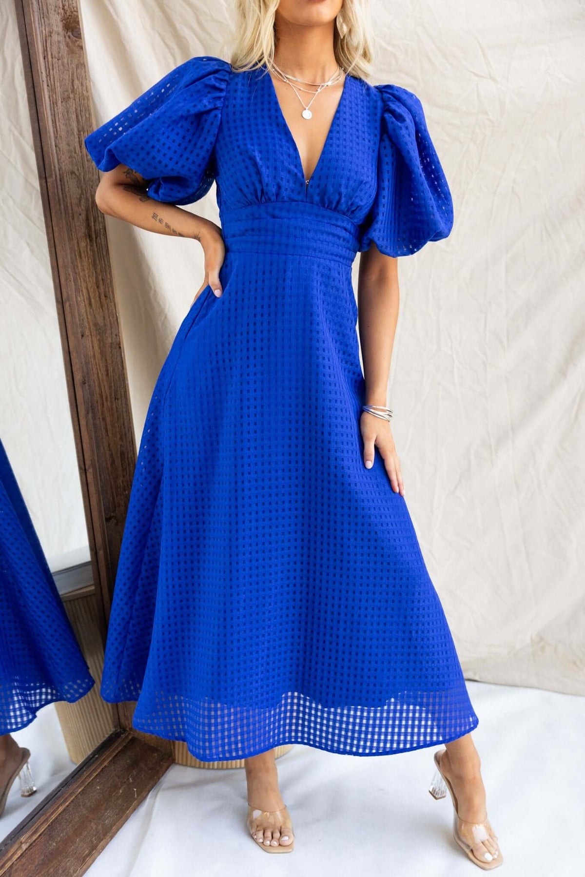 Nosita Midi Dress in vibrant blue with V-neckline, puff sleeves, pockets, and textured material, styled for a chic look.