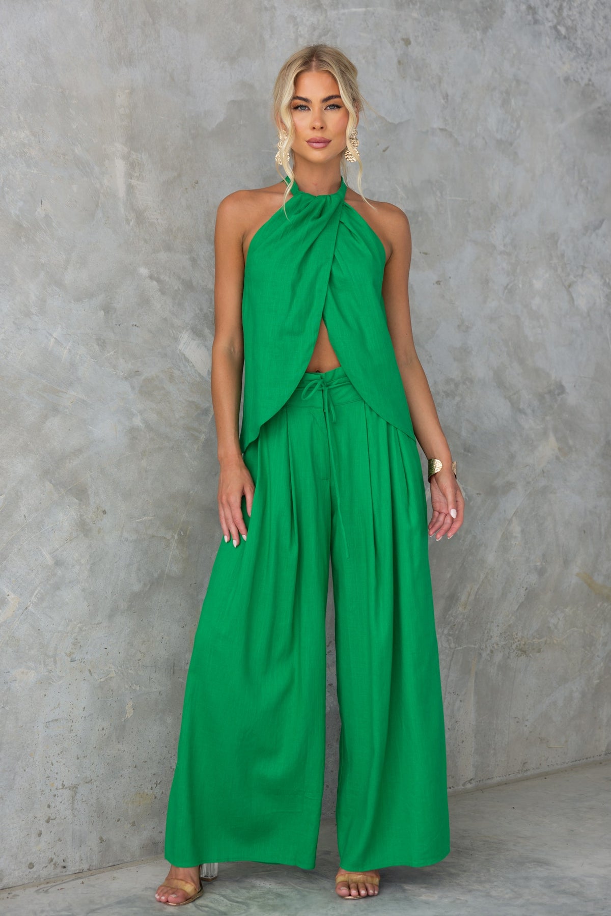 Model wearing a green Remi Top with high neckline and linen look, paired with wide-leg trousers against a textured background.